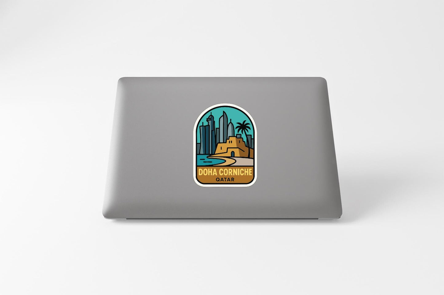 a sticker with a graphic of a cityscape and the text "Doha Corniche Qatar" on a grey laptop.