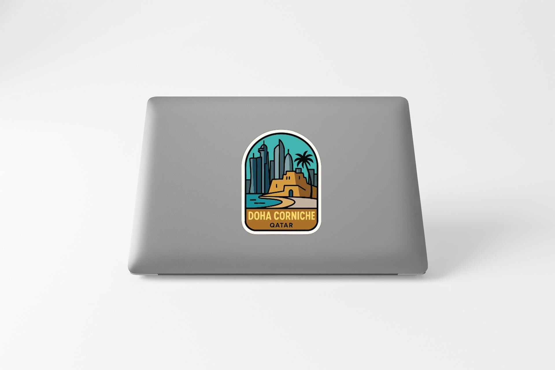 a sticker with a graphic of a cityscape and the text "Doha Corniche Qatar" on a grey laptop.