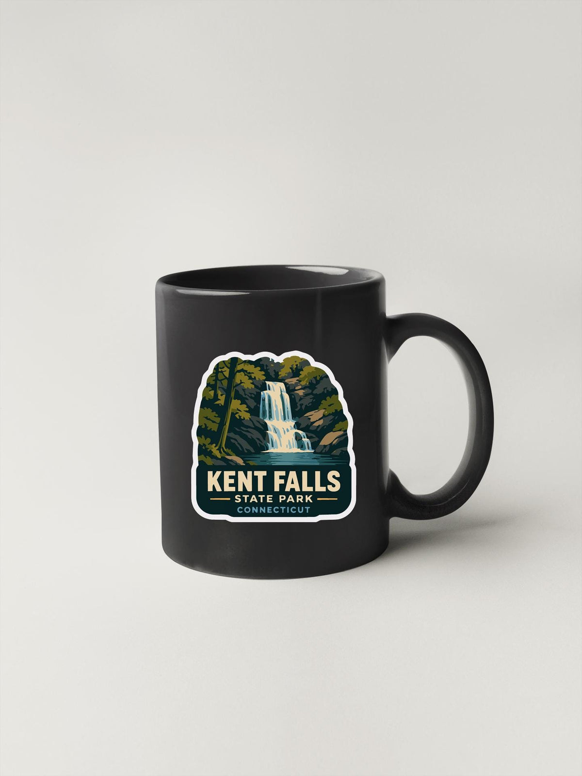 A black coffee mug with a graphic design depicting a waterfall and the text "KENT FALLS STATE PARK CONNECTICUT".