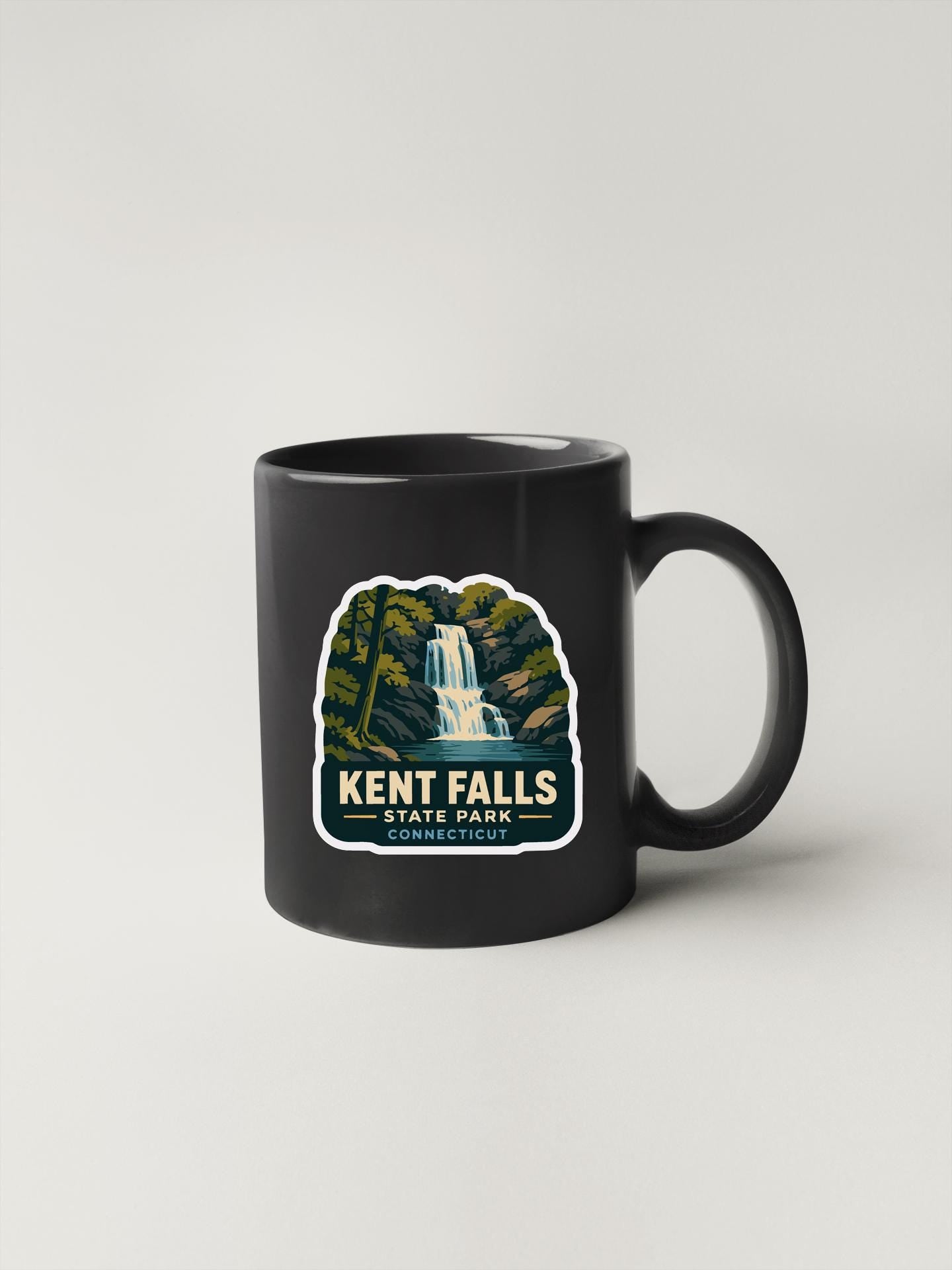 A black coffee mug with a graphic design depicting a waterfall and the text "KENT FALLS STATE PARK CONNECTICUT".