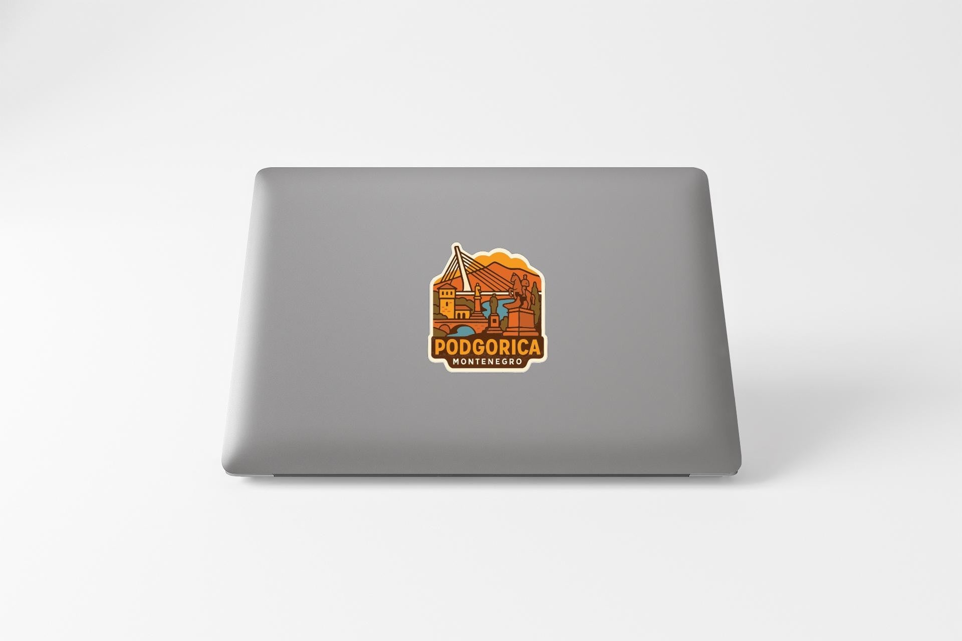a sticker on the back of a laptop with an illustration of a mountain and the text "PODGORICA" and "MANHEREIRO" printed on it.
