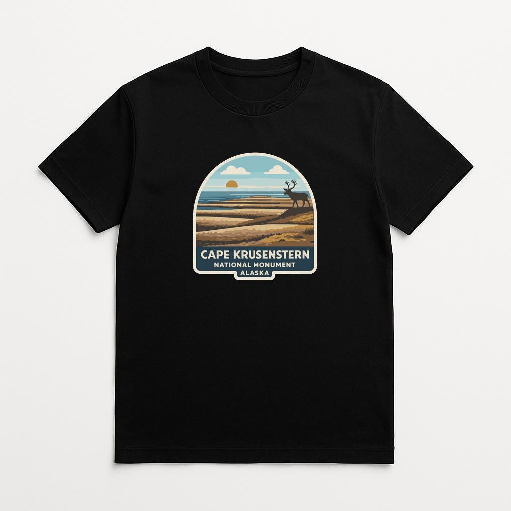 A black t-shirt with a graphic design depicting a scenic landscape with a sunset, a deer, and the text "Cape Krusenstern National Monument Alaska".