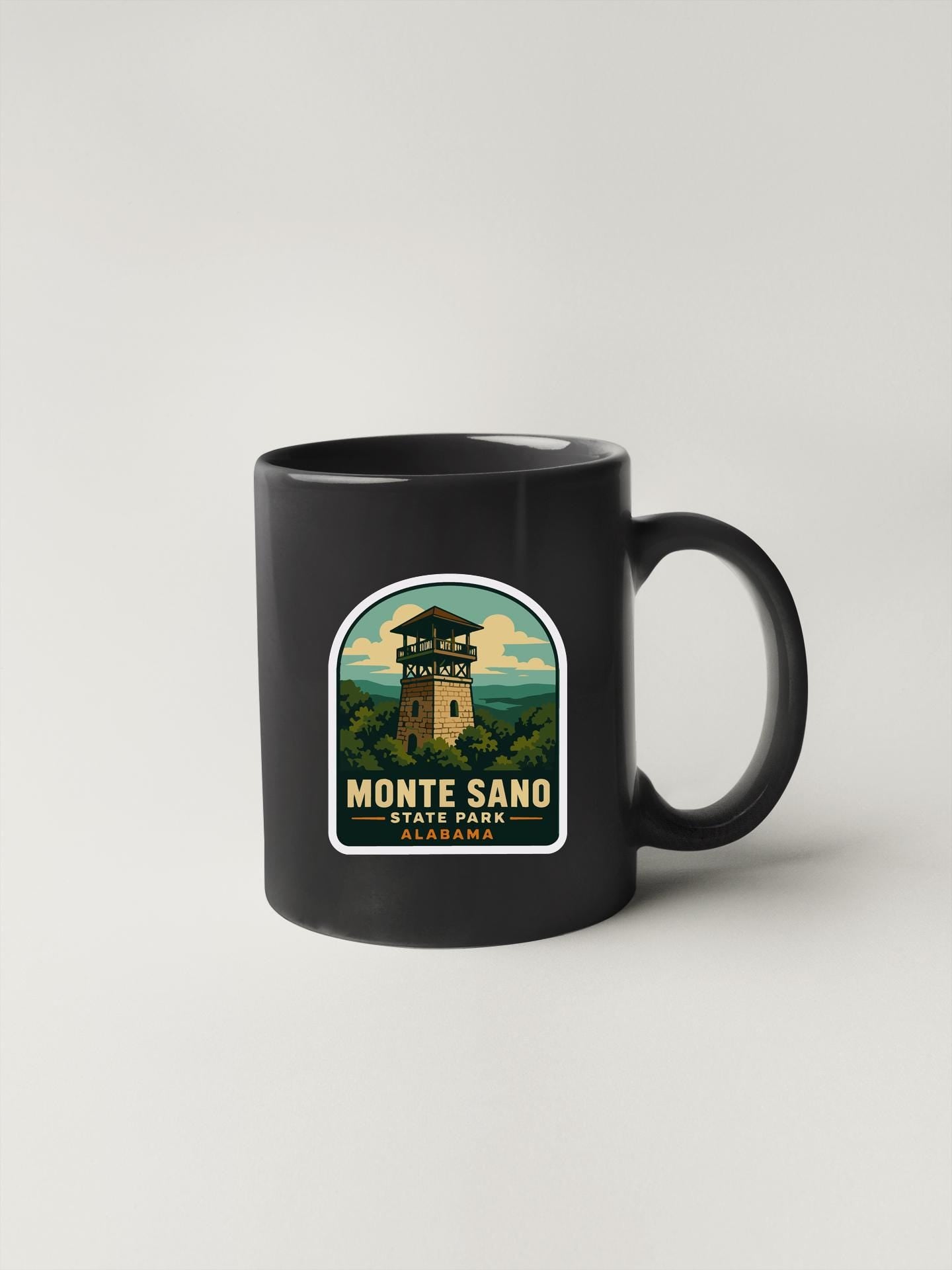 A black coffee mug with a label that says "MONTE SANO STATE PARK ALABAMA" and features an illustration of a lighthouse.