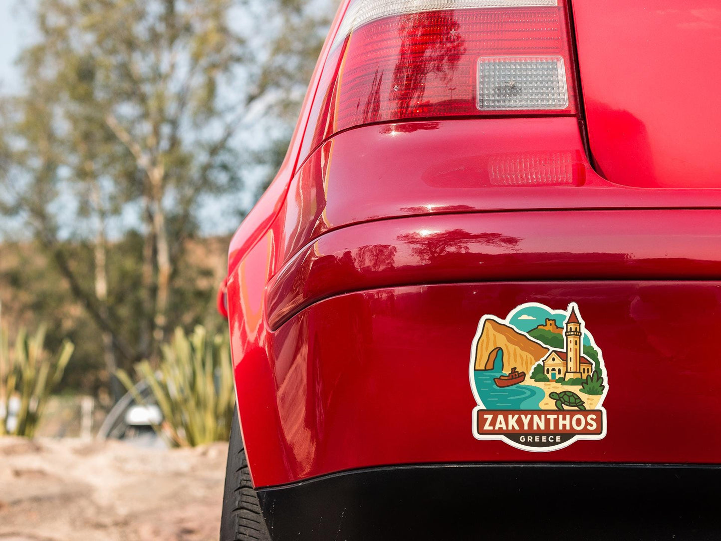 the rear end of a red car with a sticker on the trunk that features a scenic illustration of a town or village.