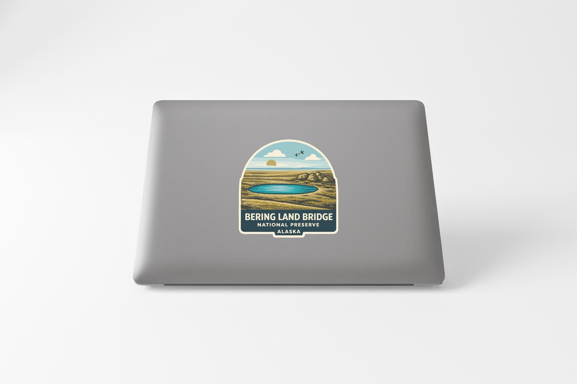 a sticker on the back of a laptop that depicts a scenic landscape with a lake and mountains.