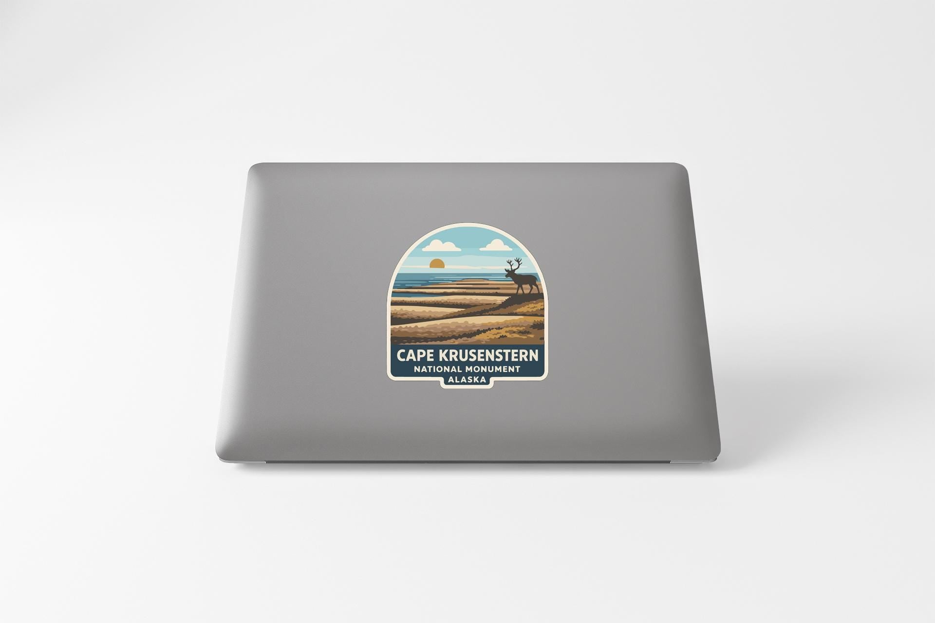 a sticker on the back of a laptop that displays a scenic landscape with a sunset, mountains, and a moose.