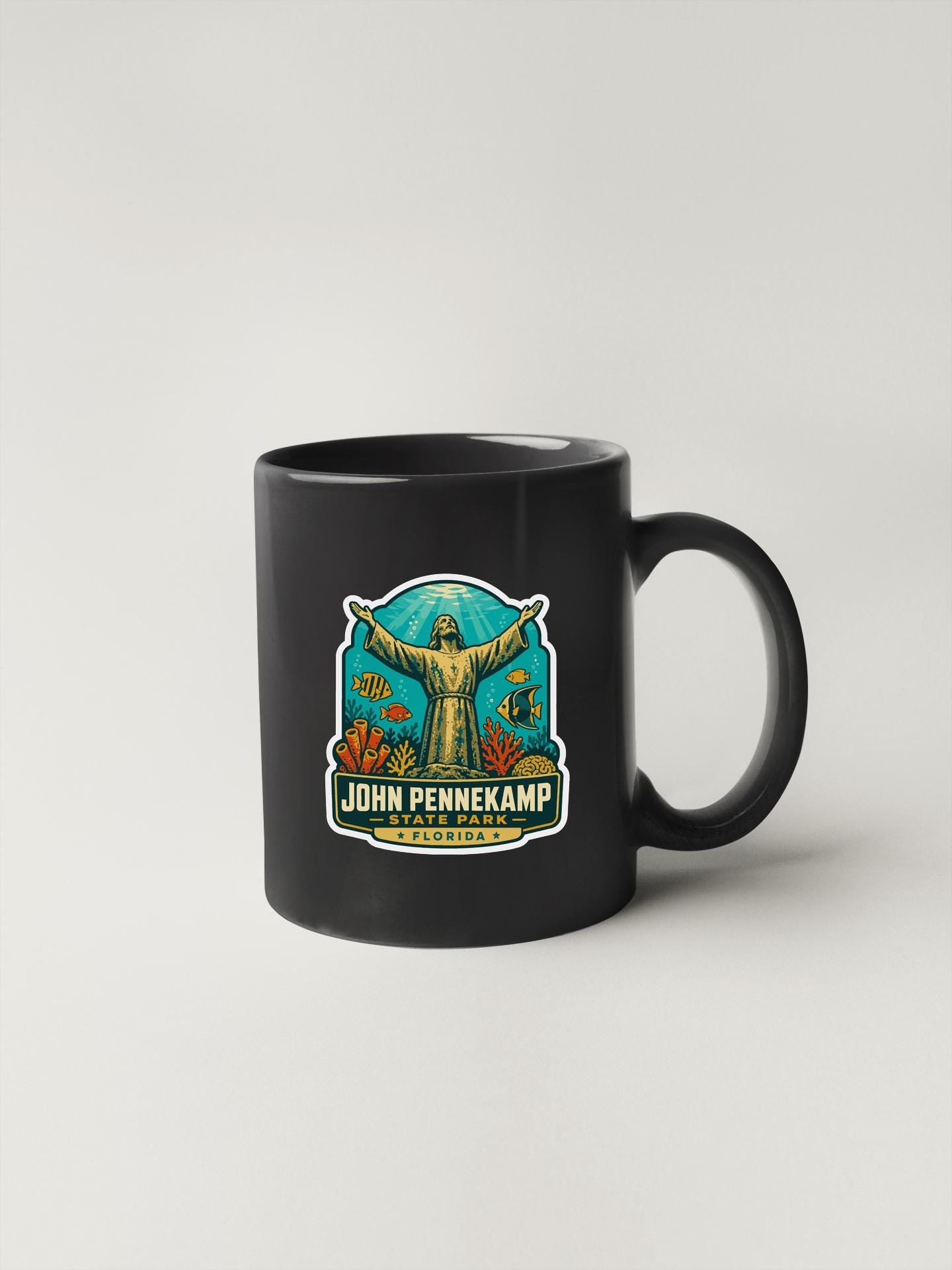 A black coffee mug with a colorful graphic design featuring a figure with outstretched arms and a background of underwater elements.