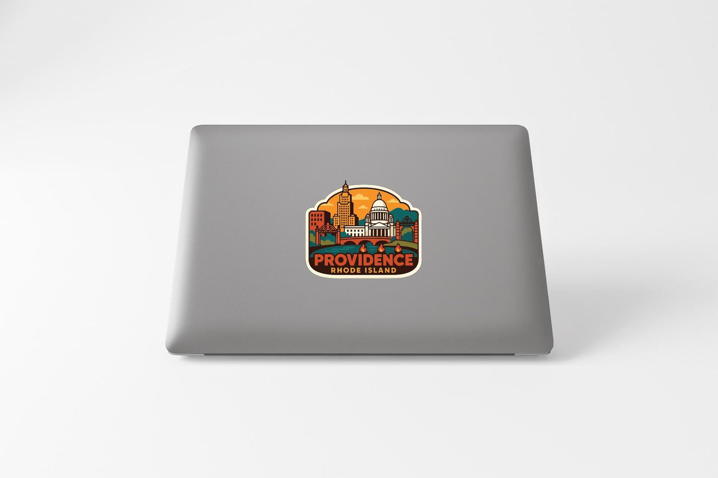 a sticker with an illustration of a cityscape and the text "PROVIDENCE, RIDGE ISLAND" on the back of a laptop.