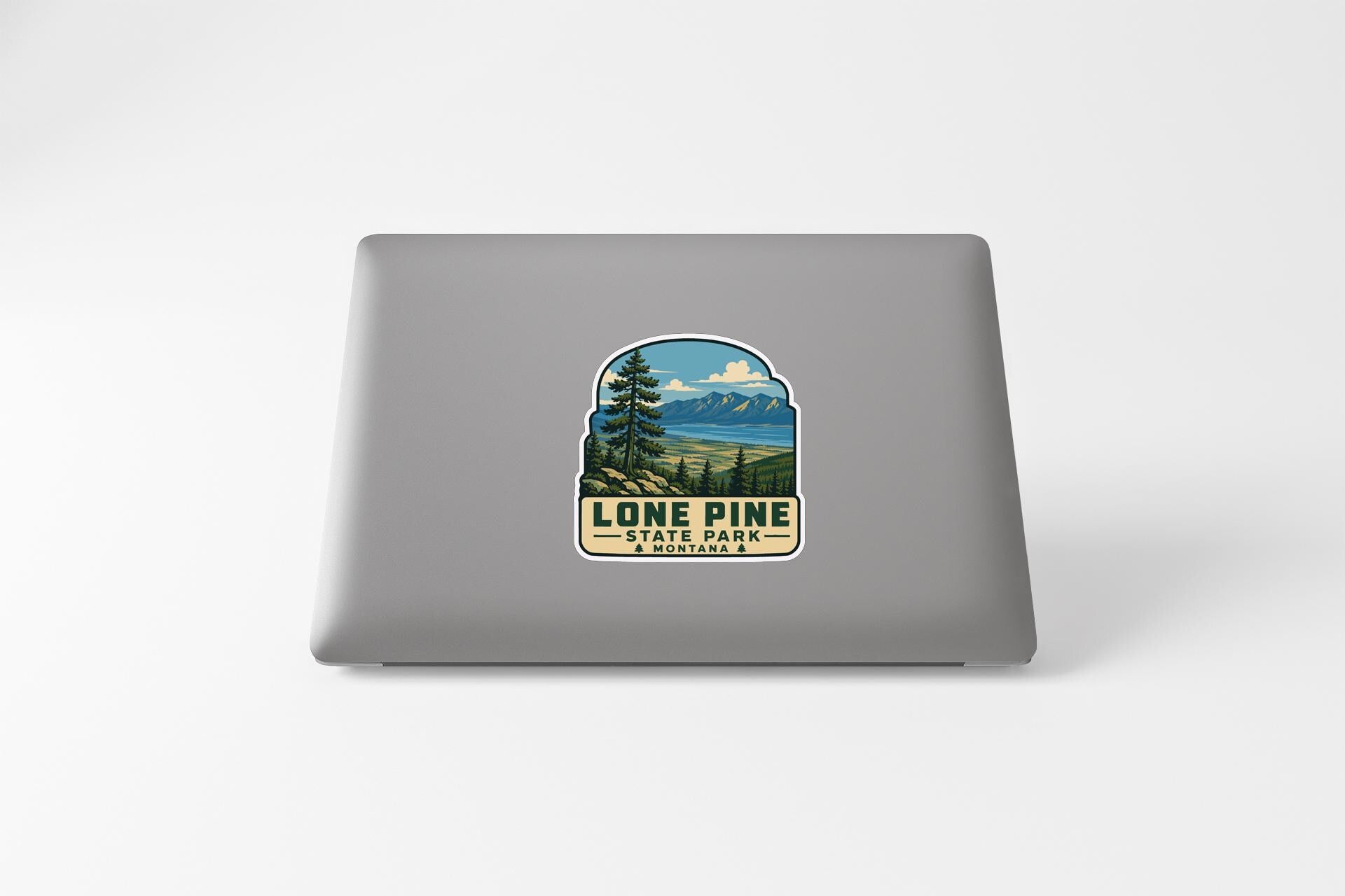 A sticker on the back of a laptop, depicting a scenic landscape with mountains, trees, and a lake.