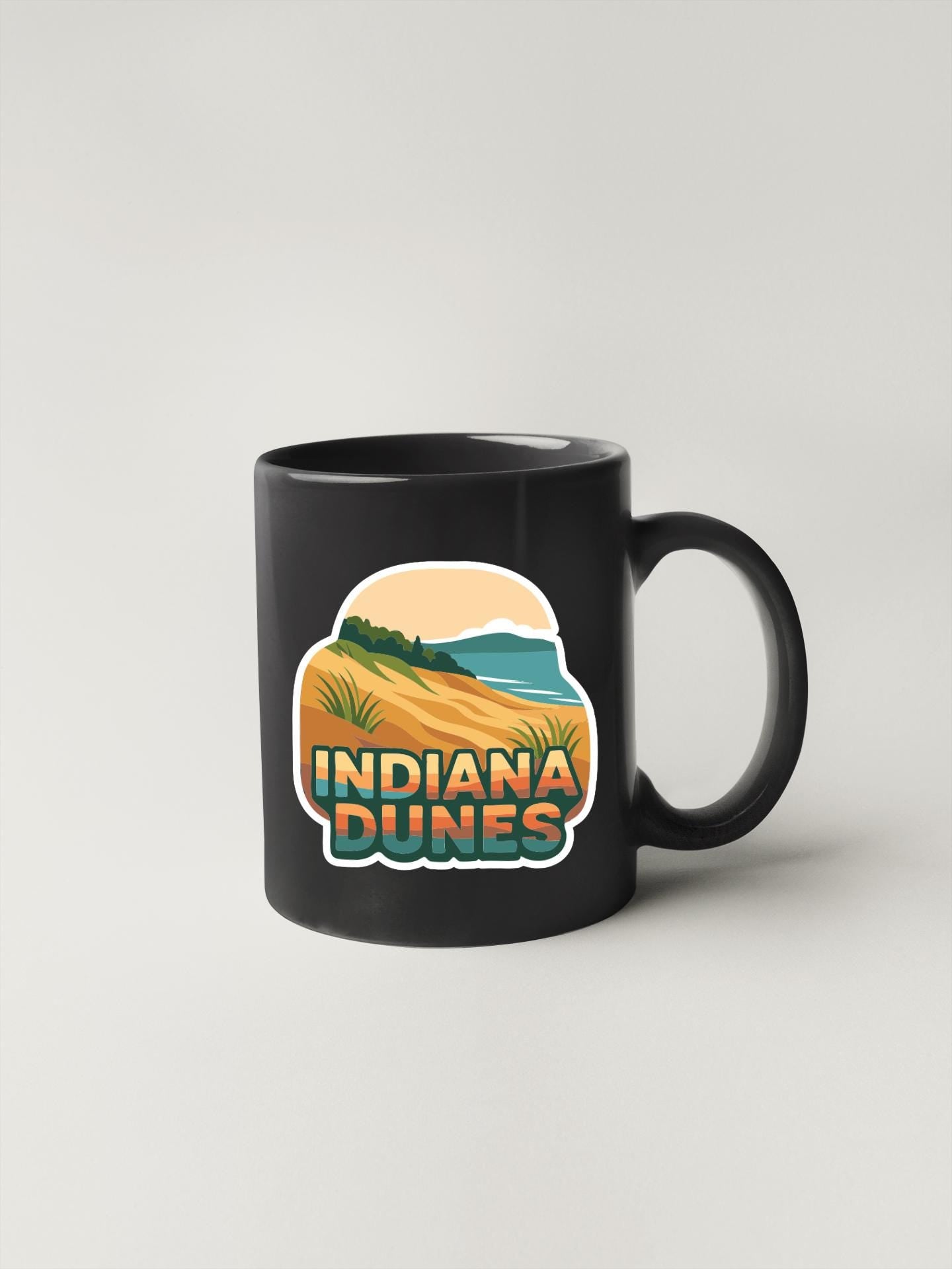 A black coffee mug with a graphic design featuring a desert landscape and the text "INDIANA DUNES" printed on it.