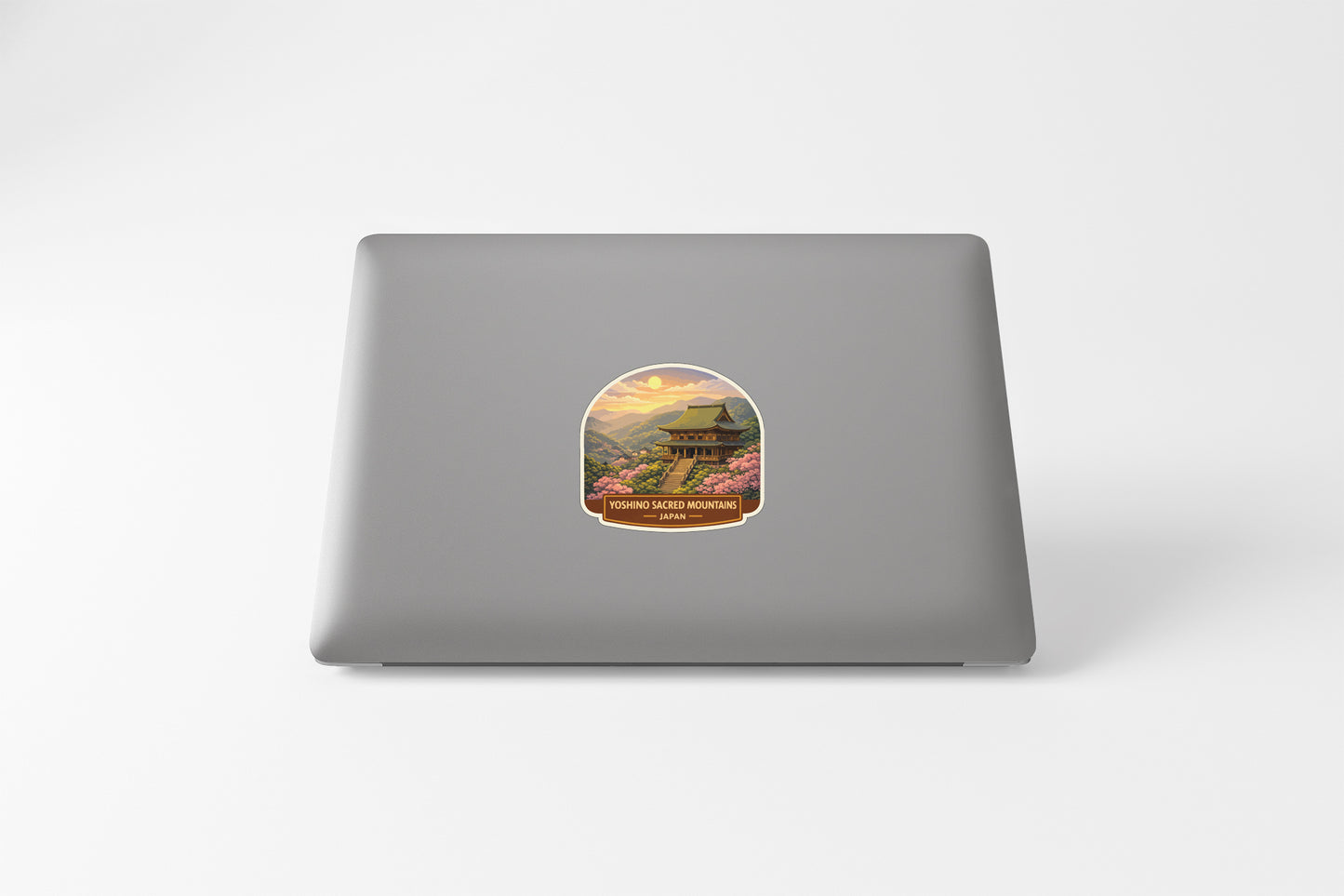A sticker depicting a temple with a sunset in the background is placed on the back of a laptop.
