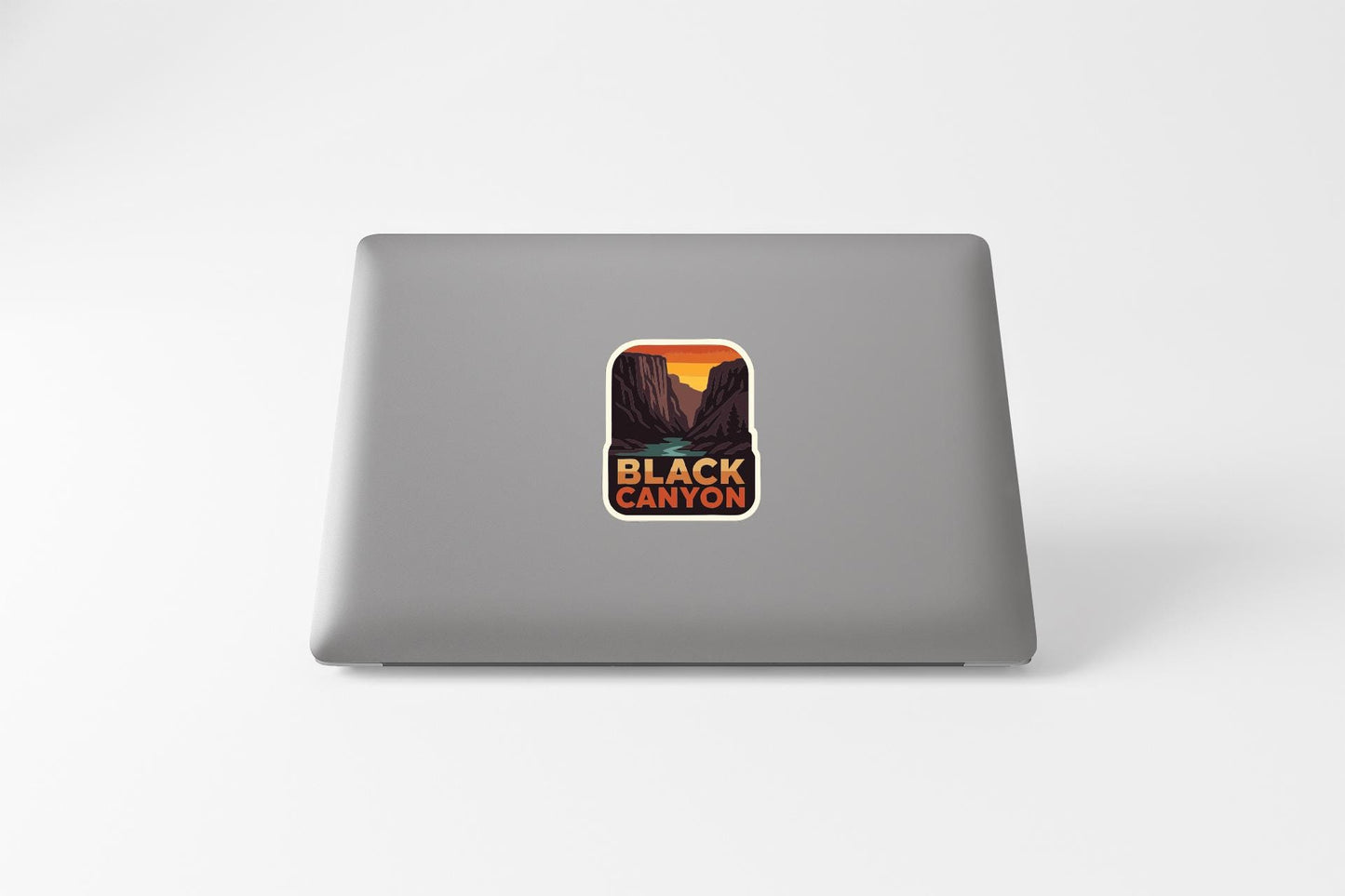 a sticker with a mountain landscape and the text "BLACK CANYON" on the back of a laptop.