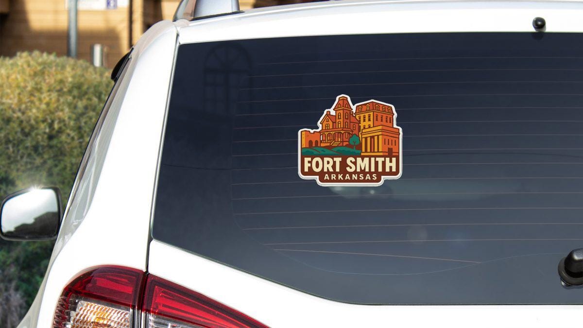 A sticker on the rear window of a white vehicle, depicting a building with a castle-like structure, indicating that the location is Fort Smith, Arkansas.