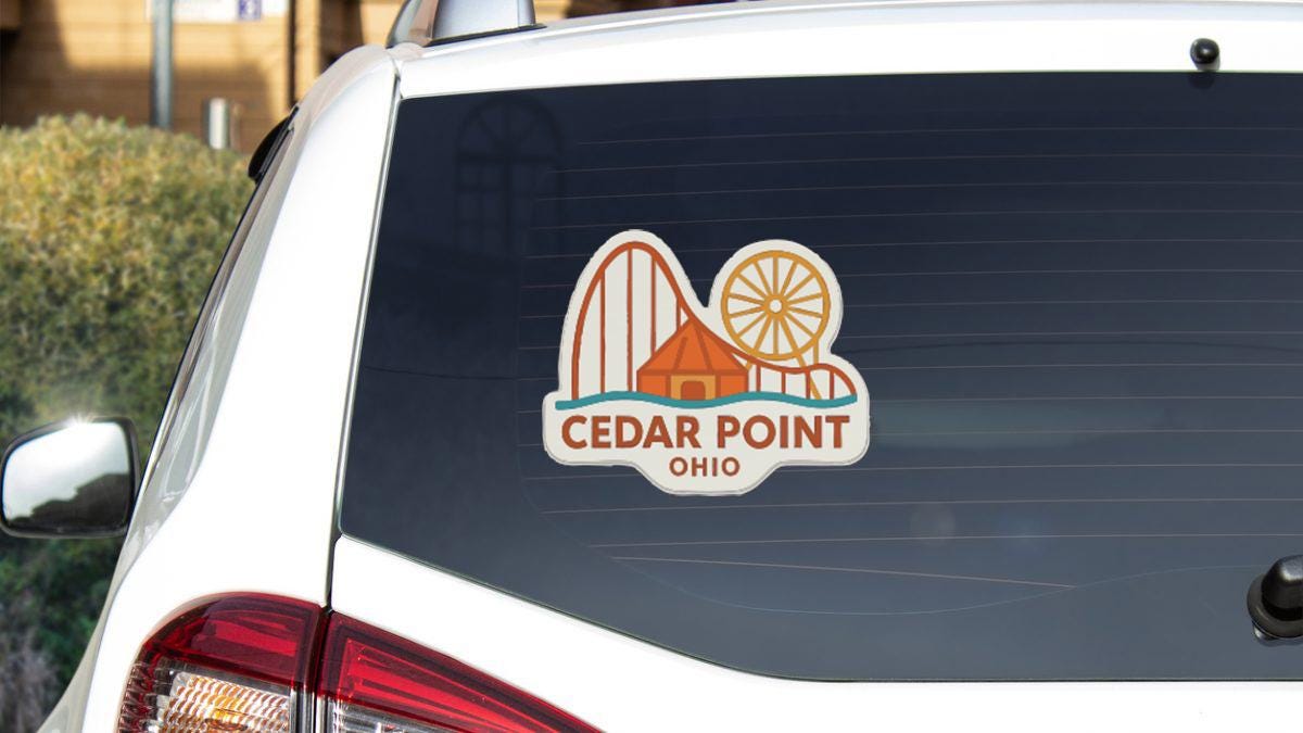 A sticker on the rear window of a white car that says "Cedar Point, Ohio".