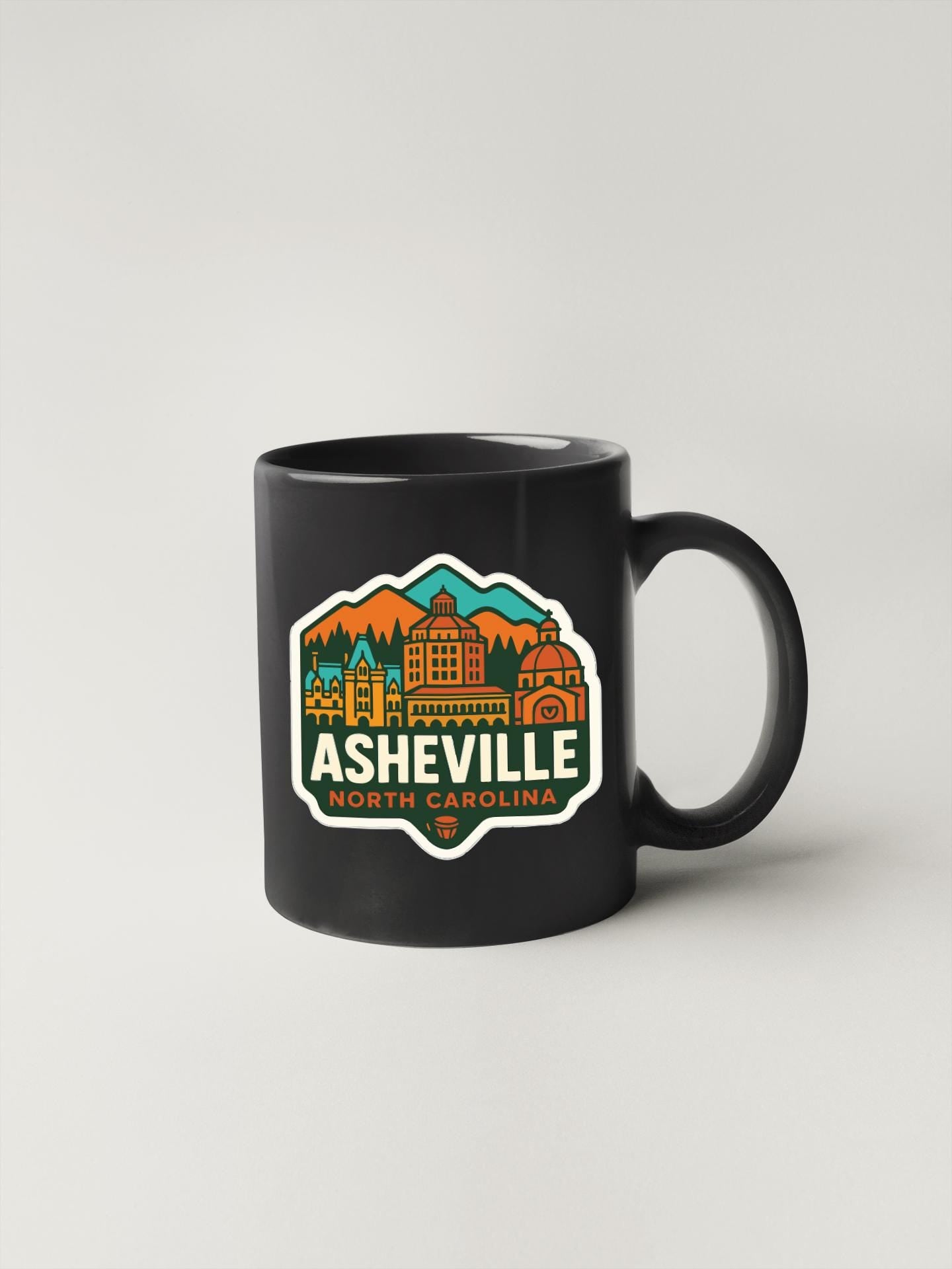 A black coffee mug with a colorful graphic design depicting the city of Asheville, North Carolina.