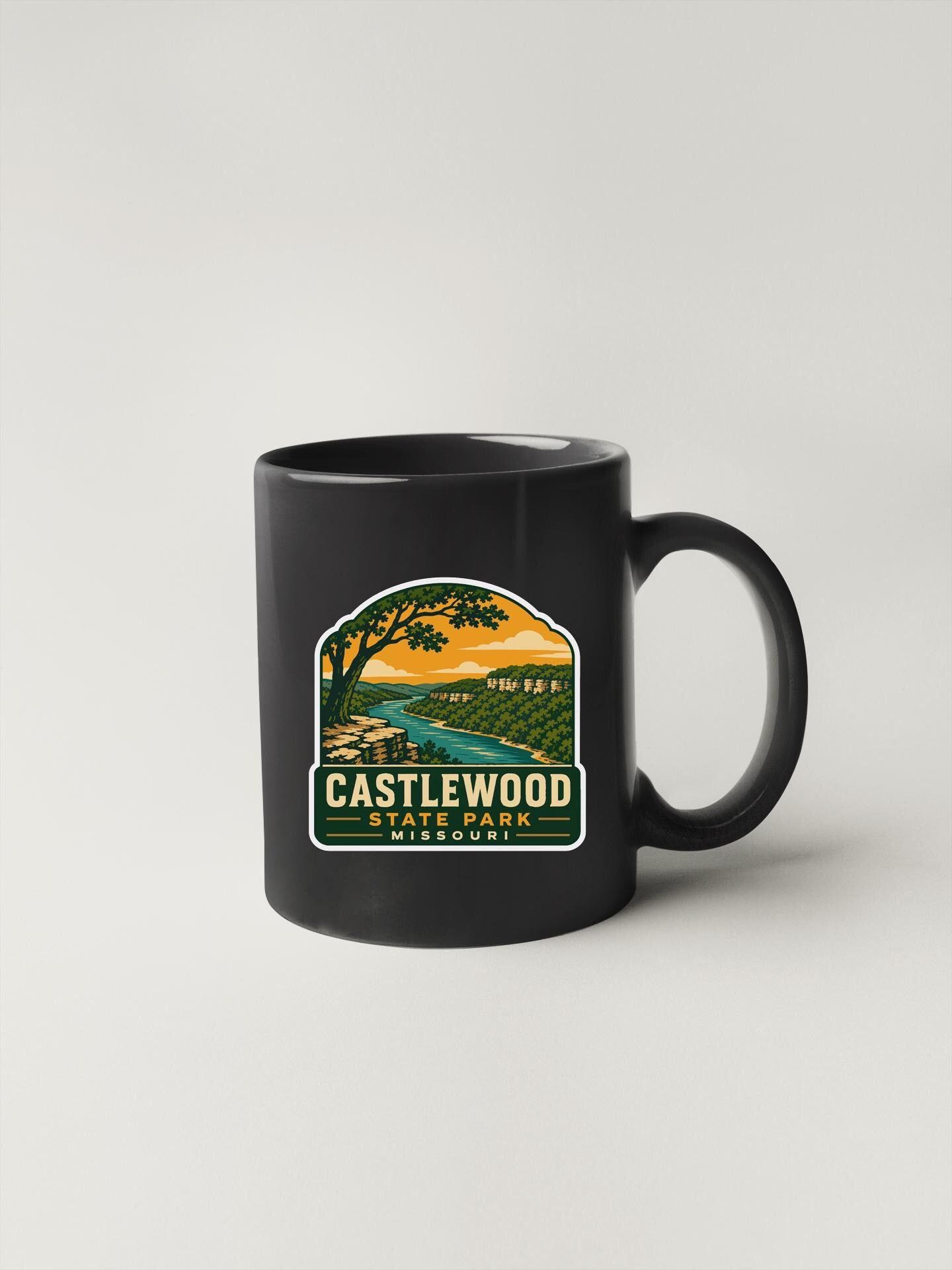 A black coffee mug with a graphic design depicting a scenic landscape, including a river, trees, and a sunset.