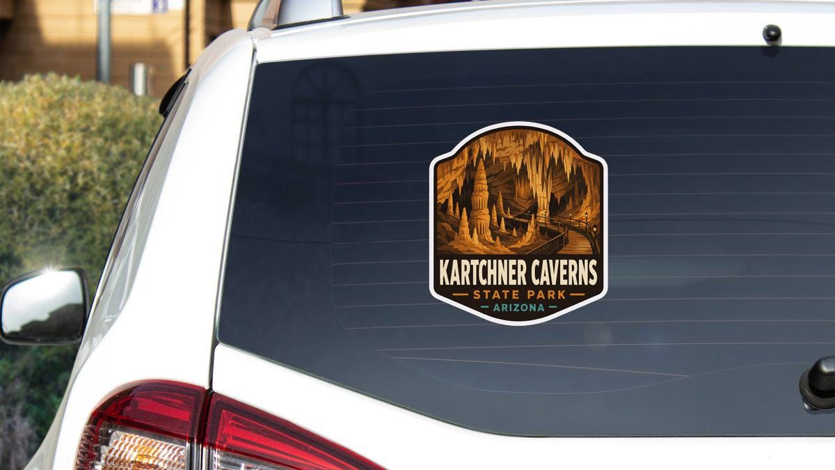 A sticker on the rear window of a white vehicle, depicting the entrance to Karchner Caves in Arizona.