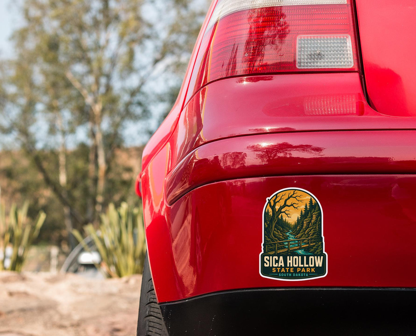the rear end of a red car with a sticker on the trunk that says "SICA HOLOWE State Park South Dakota".