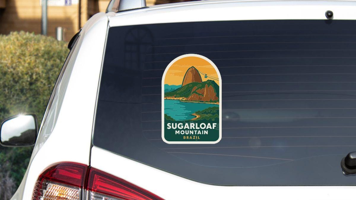 a sticker on the rear window of a white car, depicting Sugarloaf Mountain in Brazil.