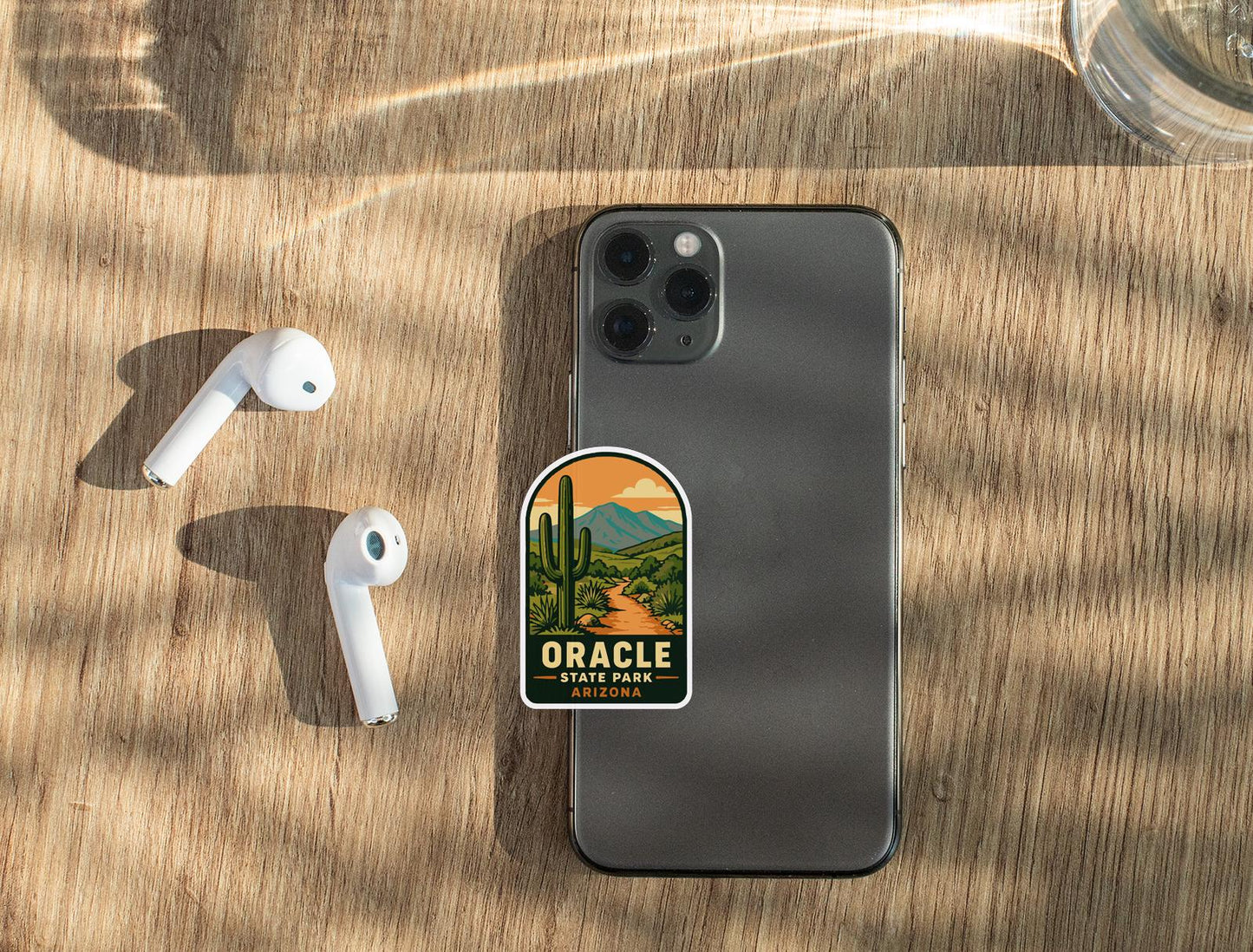 a smartphone with a sticker on it, along with a pair of white earbuds and a glass of water on a wooden surface.