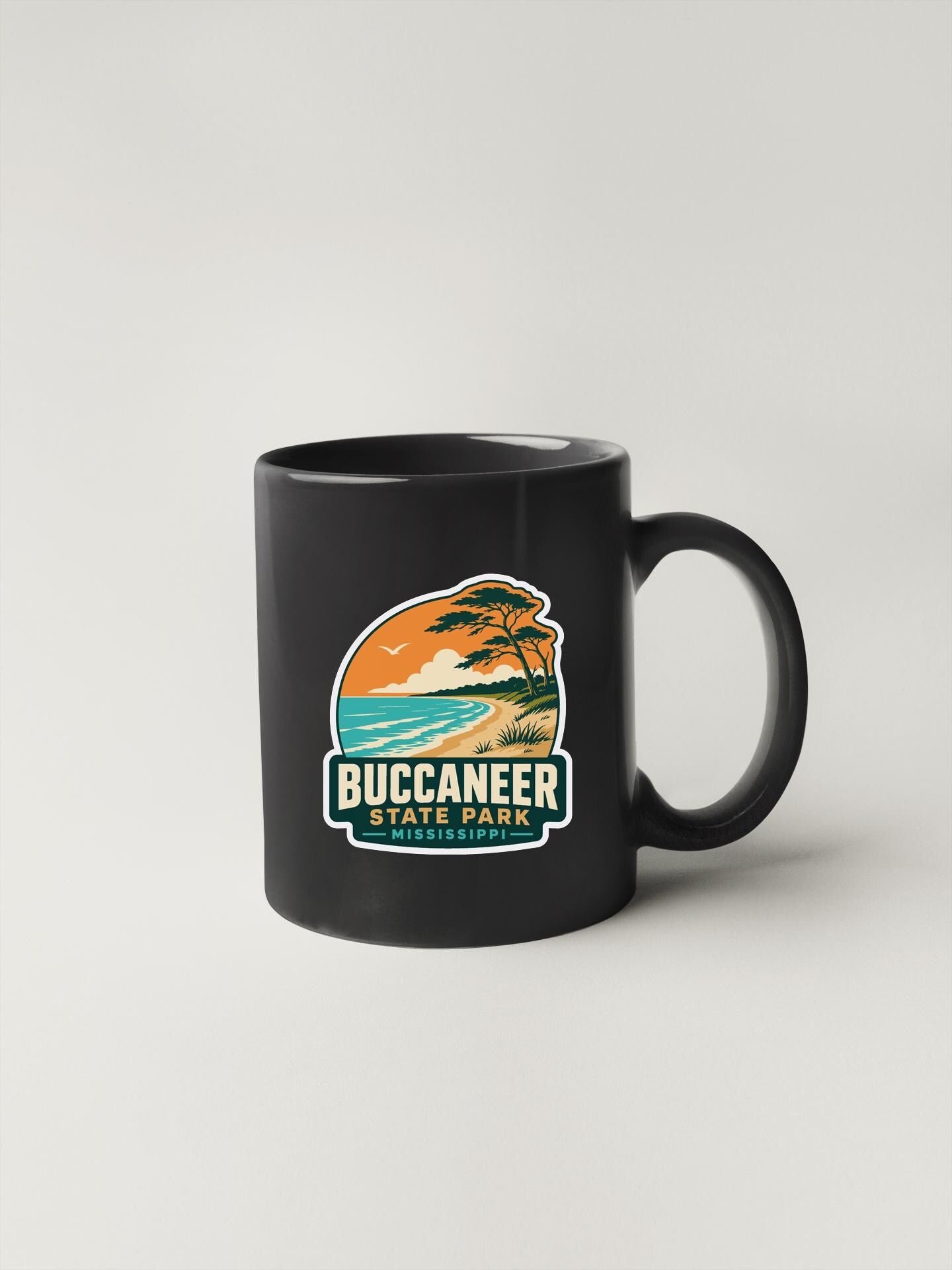 A black coffee mug with a graphic design depicting a beach scene and palm trees, along with the text "BUCCANEEER STATE PARK" printed on it.
