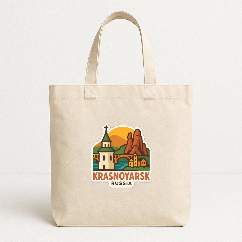 A beige tote bag with a graphic design depicting a scenic landscape with mountains, buildings, and a church.