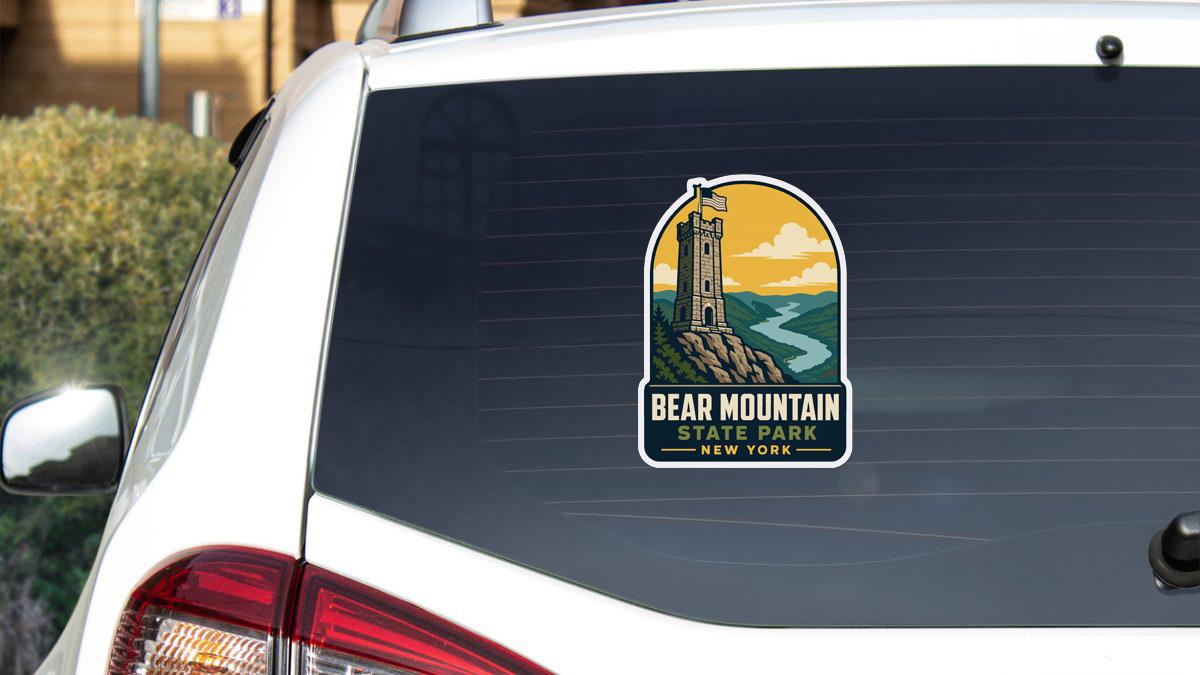 A sticker on the rear window of a white car, depicting a lighthouse and the text "BEAR MOUNTAIN STATE PARK NEW YORK".