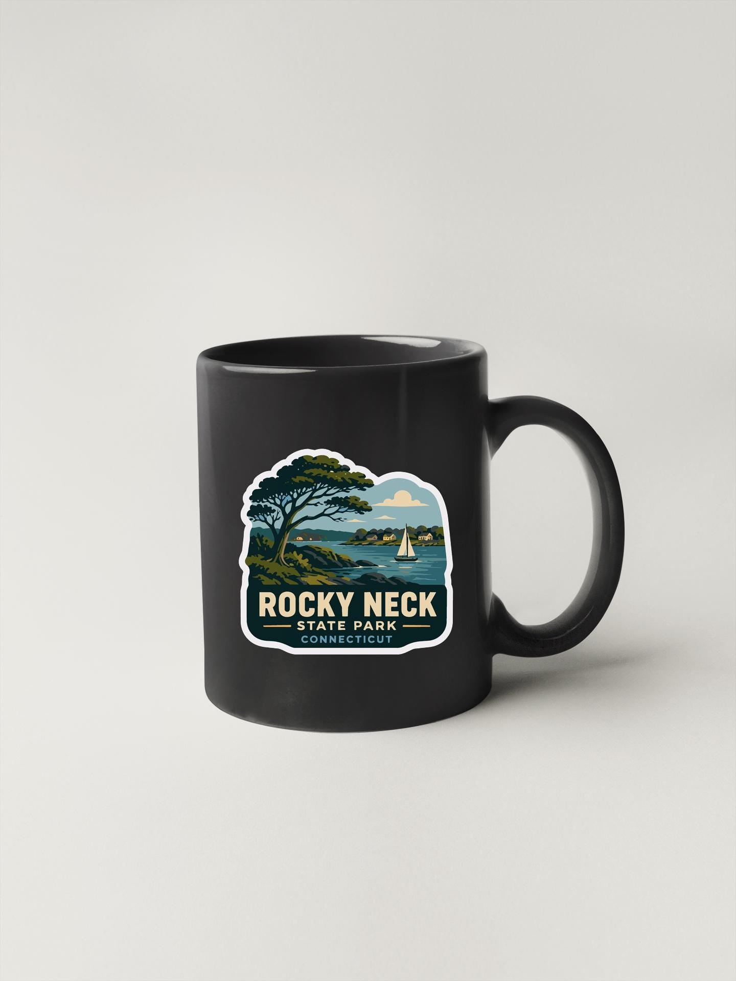 A black coffee mug with a sticker depicting Rocky Neck State Park and a sailboat in the water.