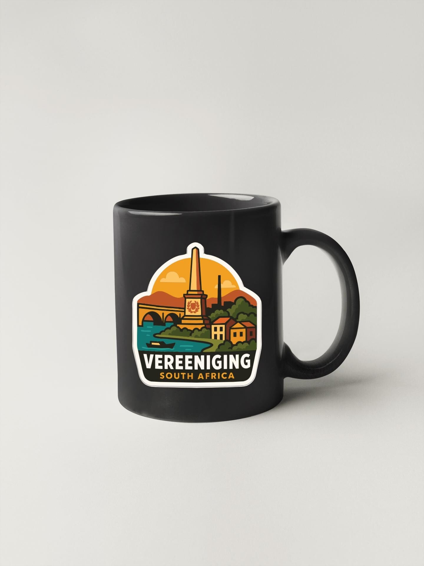 A black coffee mug with a colorful sticker depicting a cityscape and the text "Vereeniging South Africa".