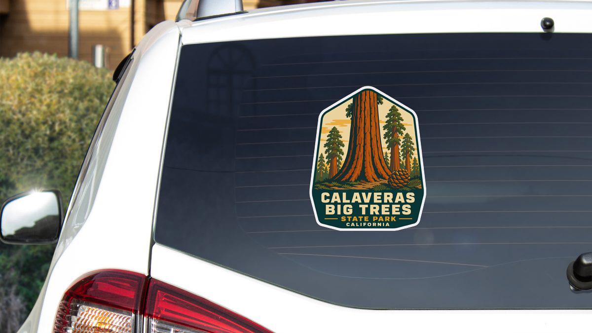 A sticker on the rear window of a white car, depicting a scenic image of the Calaveras Big Trees State Park in California.