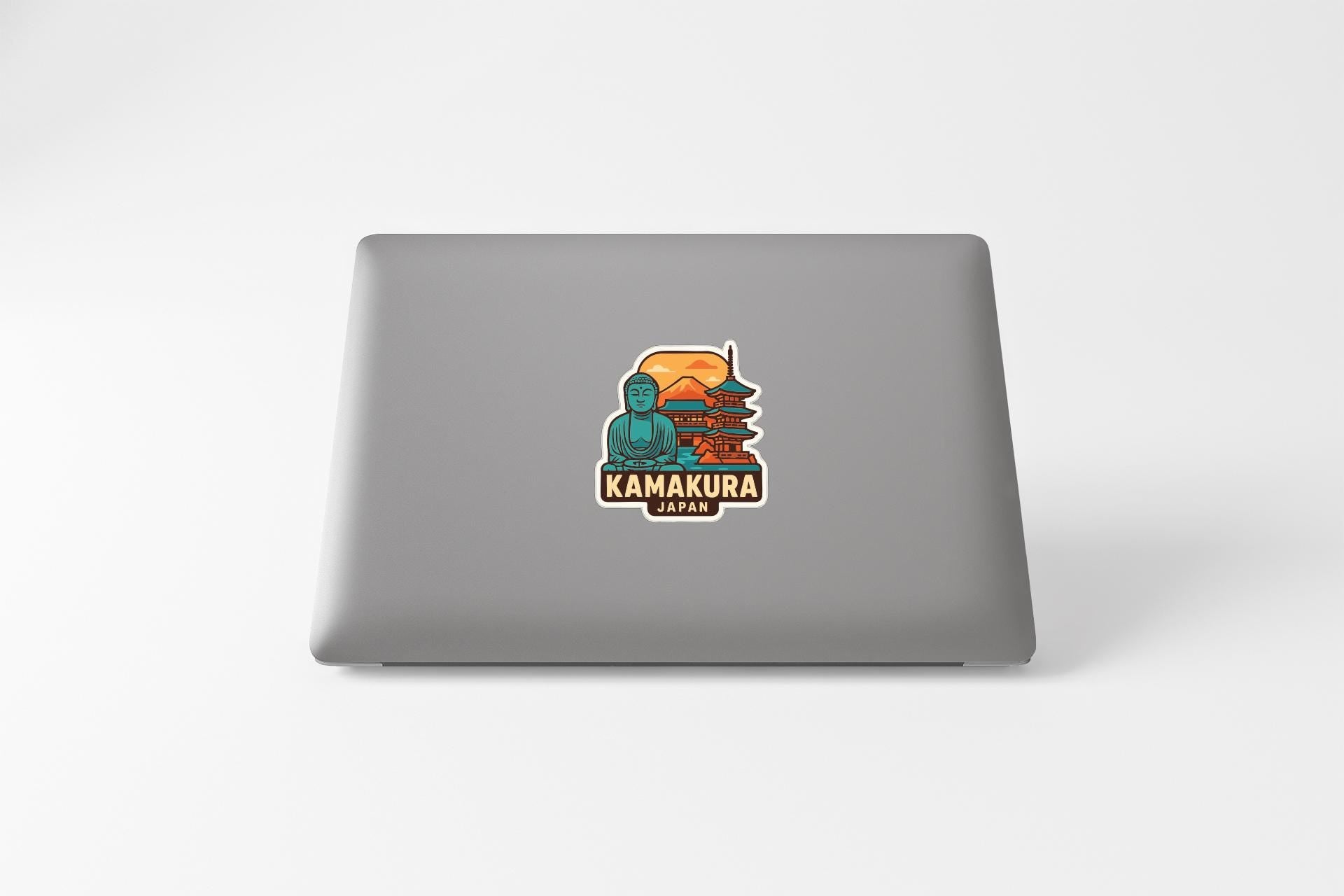 A sticker on the back of a laptop displaying a colorful illustration of a temple and a Buddha statue, with the text "KAMKURA JAPAN" below it.
