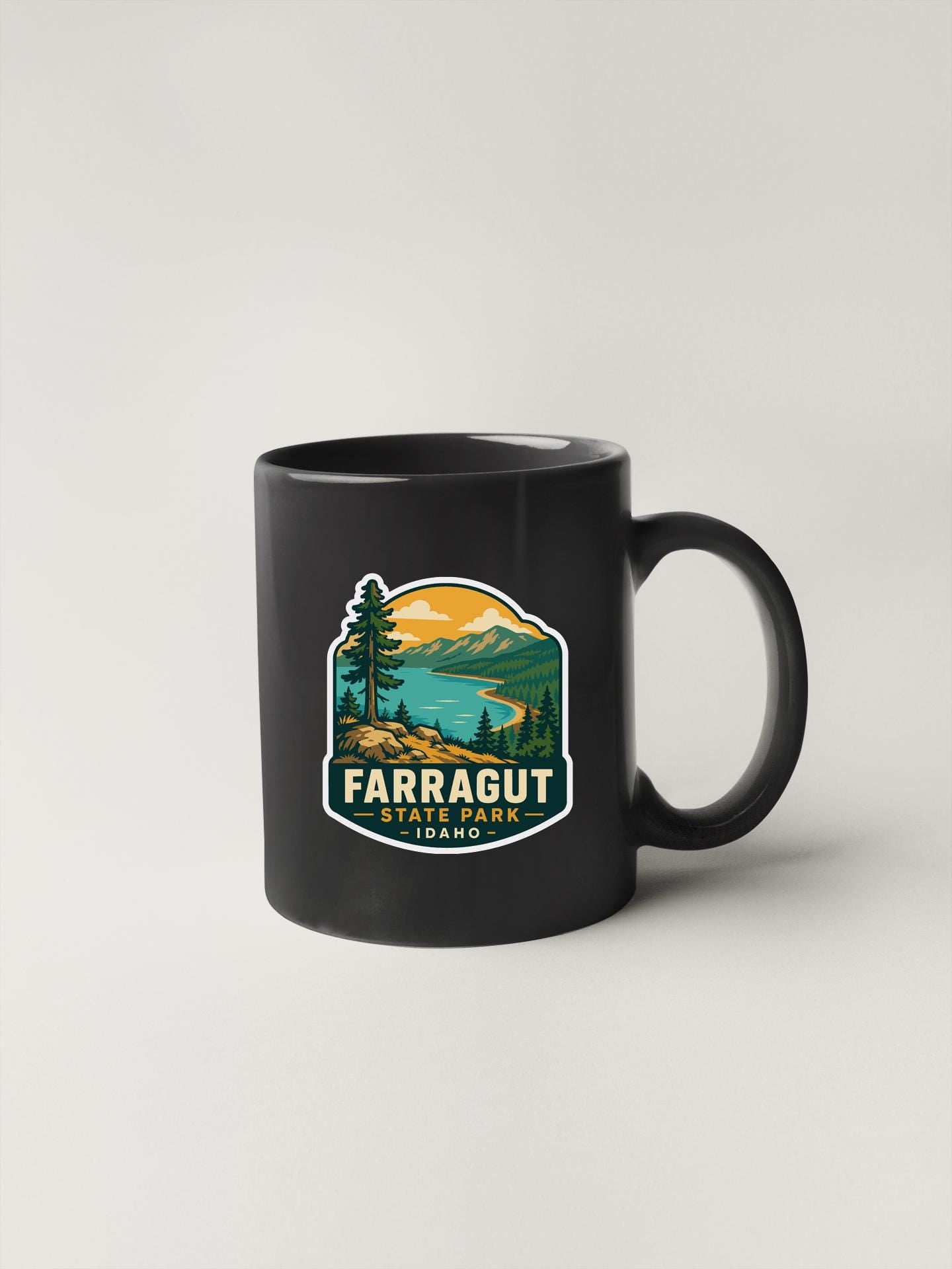 A black coffee mug with a graphic design depicting a scenic landscape, including mountains, trees, and a lake.