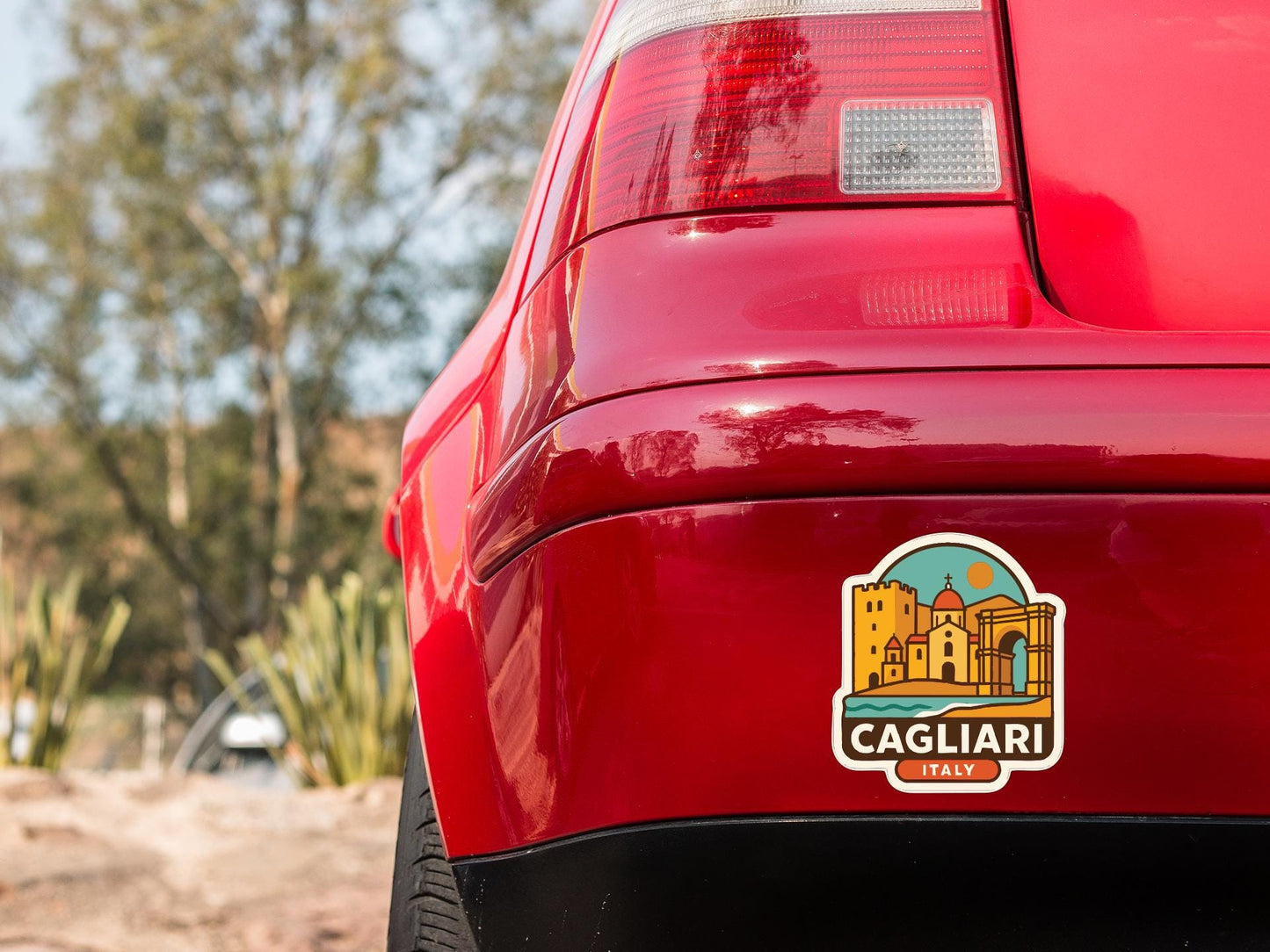 the rear end of a red car with a sticker on the trunk that says "Cagliari Italy".