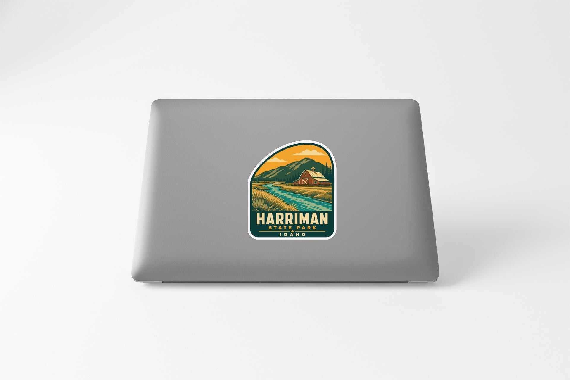 A sticker on the back of a laptop, depicting a scenic landscape with mountains, a river, and a small building.