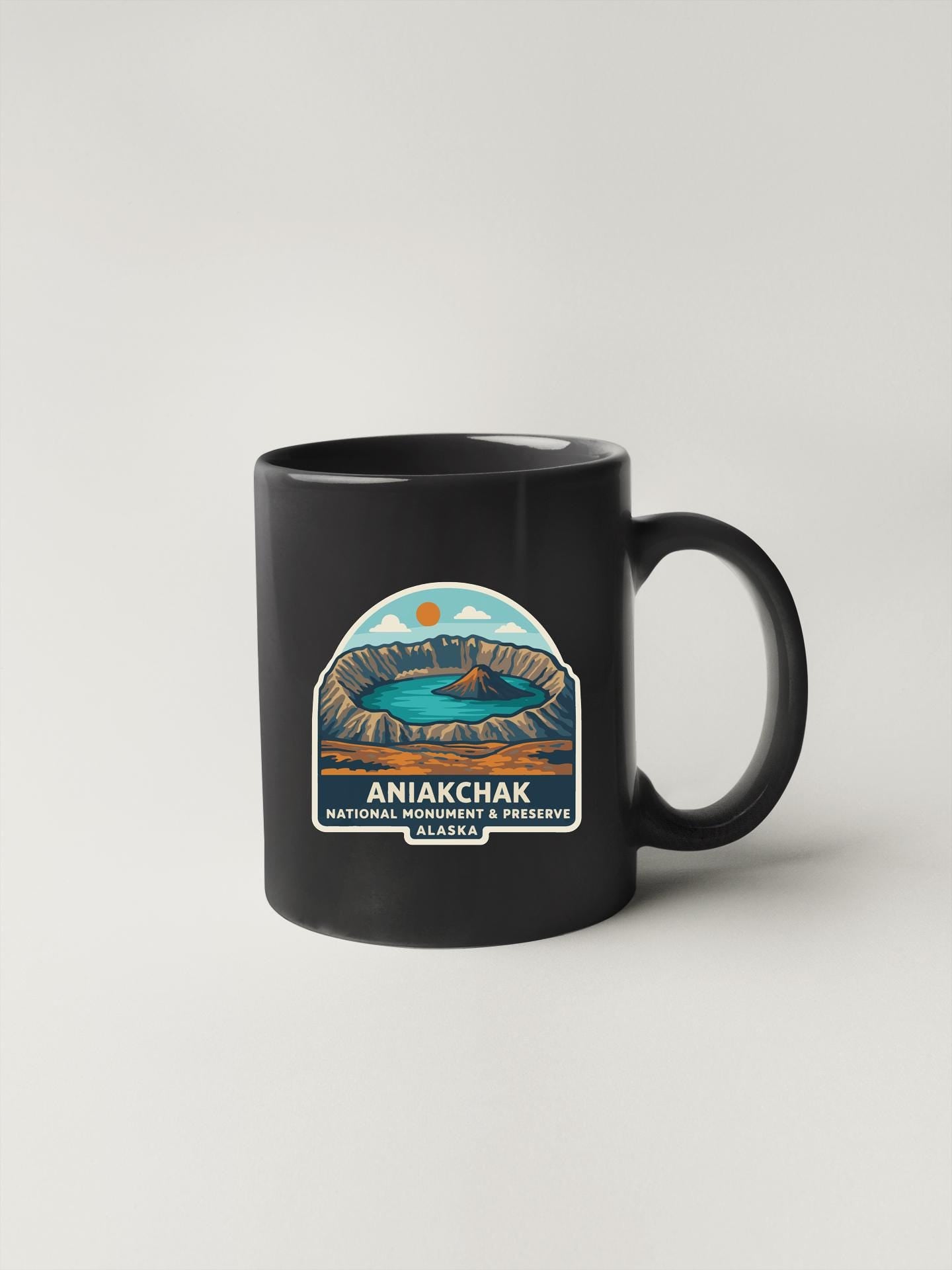 A black coffee mug with a graphic design depicting the Aniakchak National Monument and Preserve in Arizona.