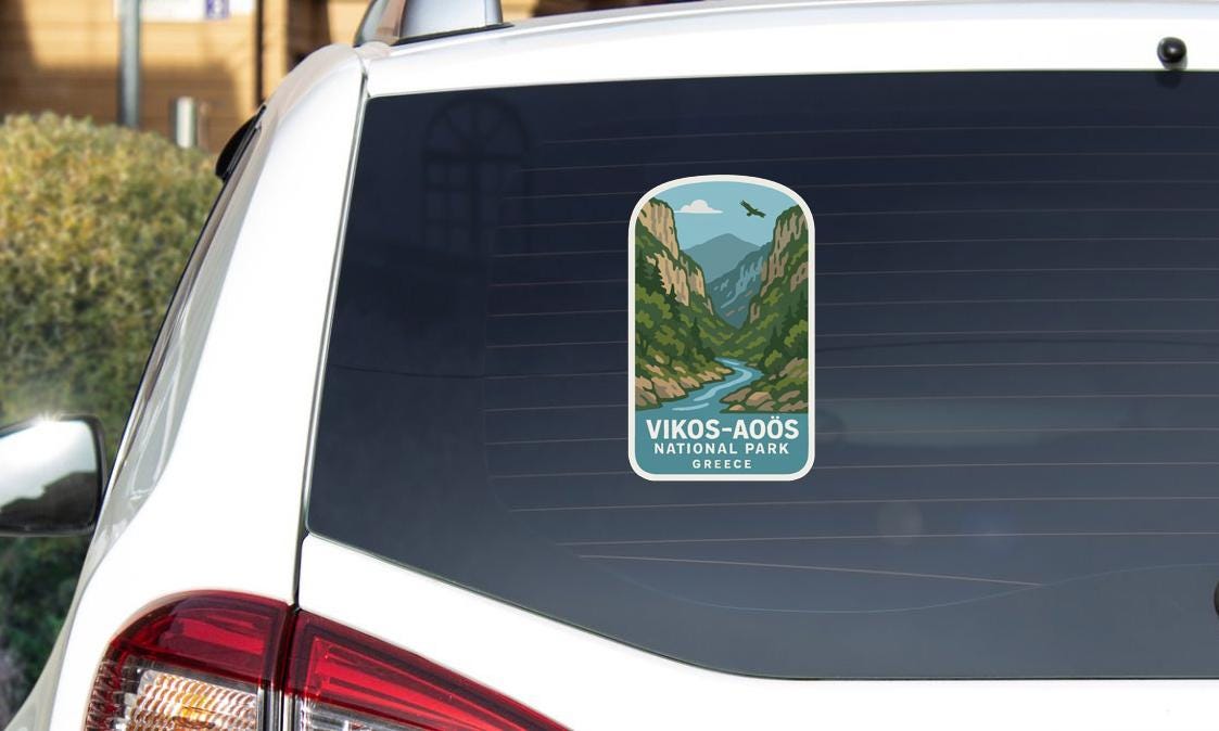 A sticker on the rear window of a white car, depicting a scenic mountain landscape with a winding river.