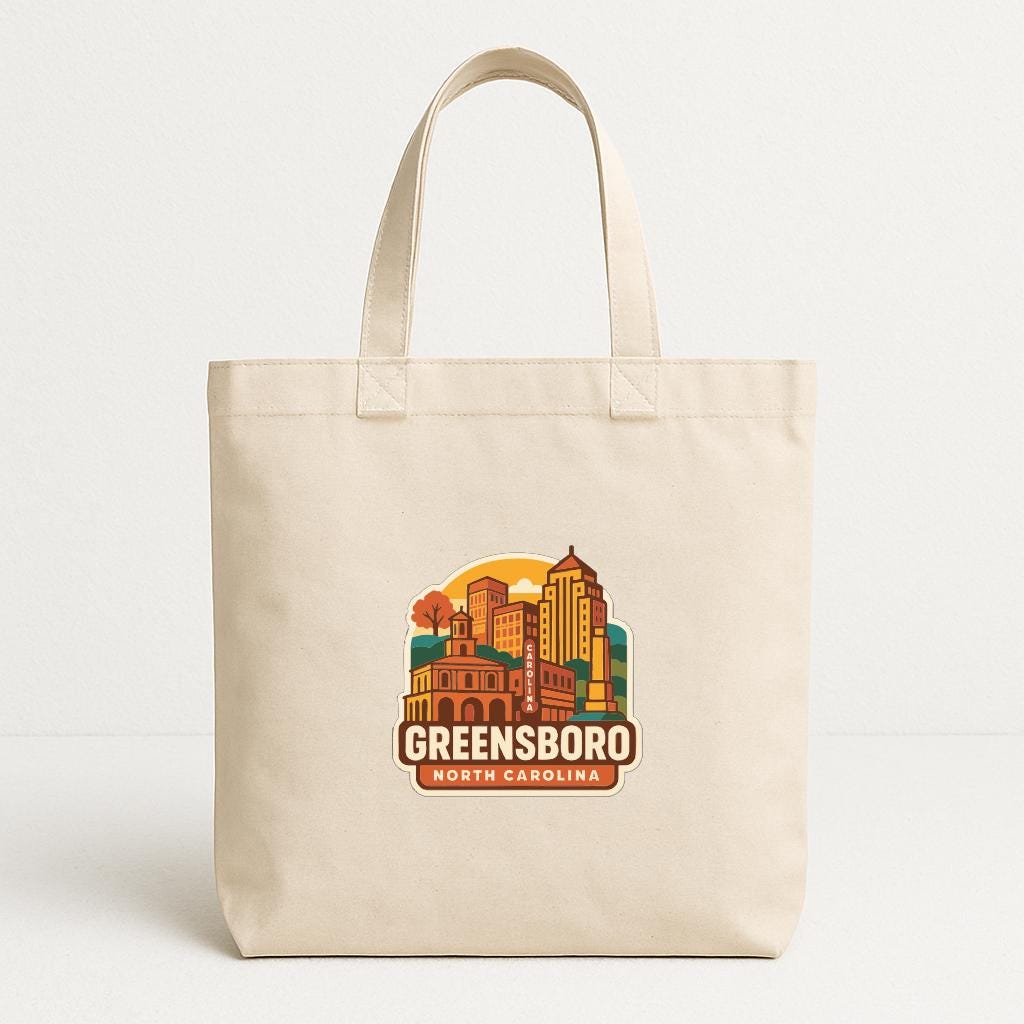 A beige tote bag with a printed design of a city skyline and the text "GREENSBORO NORTH CAROLINA" printed on it.