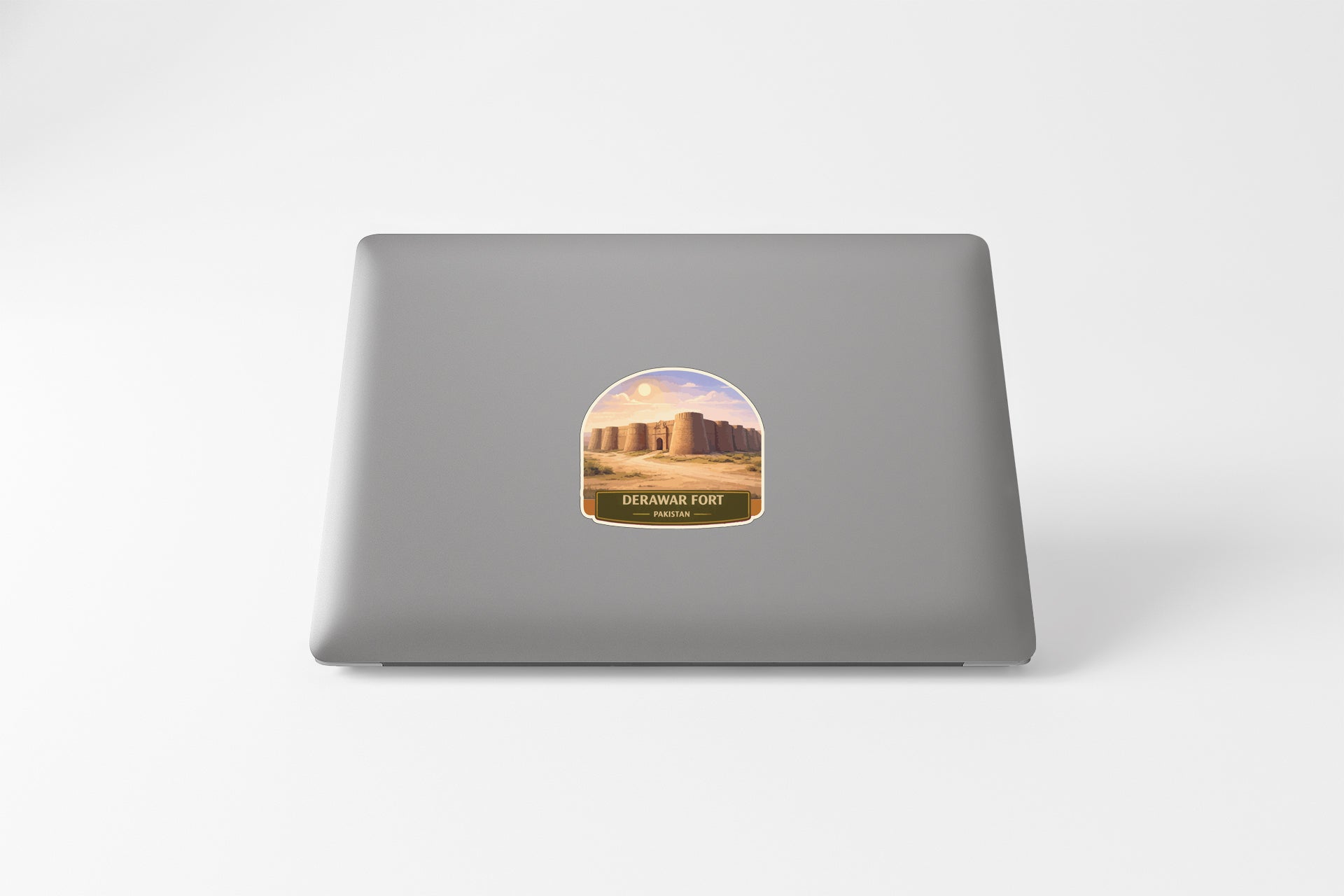 a sticker on the back of a laptop, depicting a desert landscape with a castle or fort in the background.