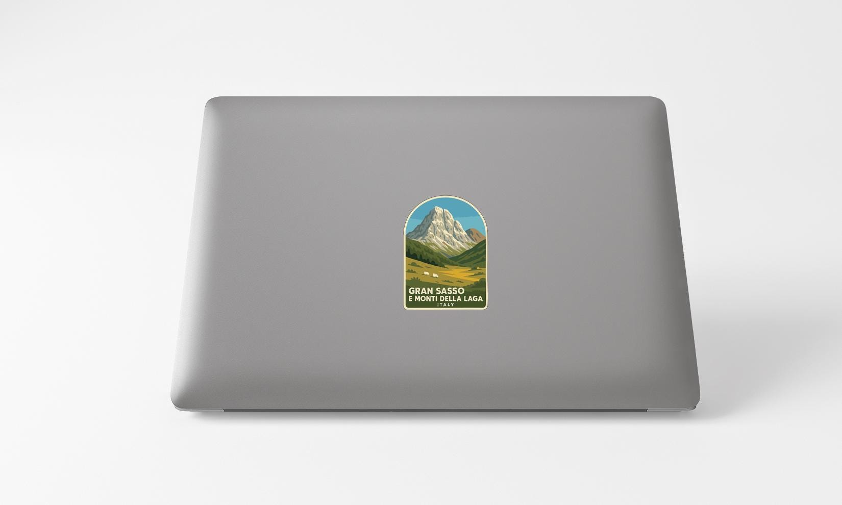 A sticker depicting a mountain landscape with the text "GRAN SASSO" and "MONTICELLA LAGA" printed on a grey laptop.