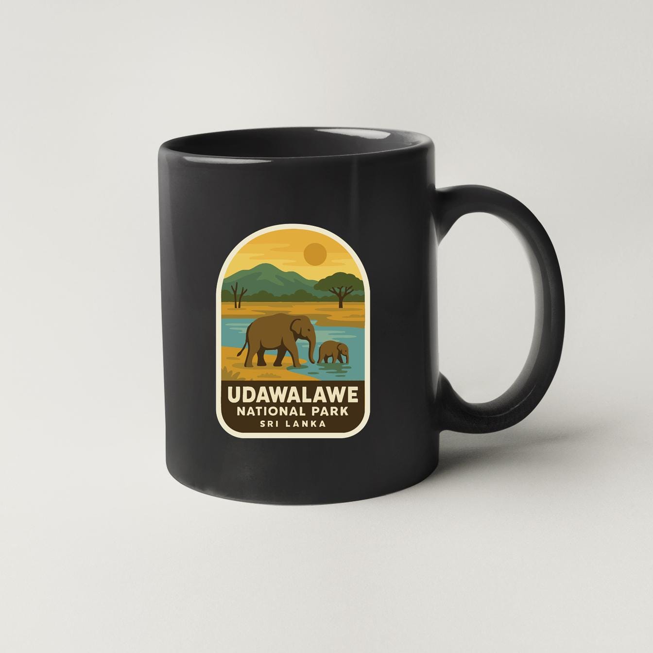 A black coffee mug with a label that features an illustration of elephants in a natural setting, along with the text "UDAWALAVE NATIONAL PARK SRI LANKA".