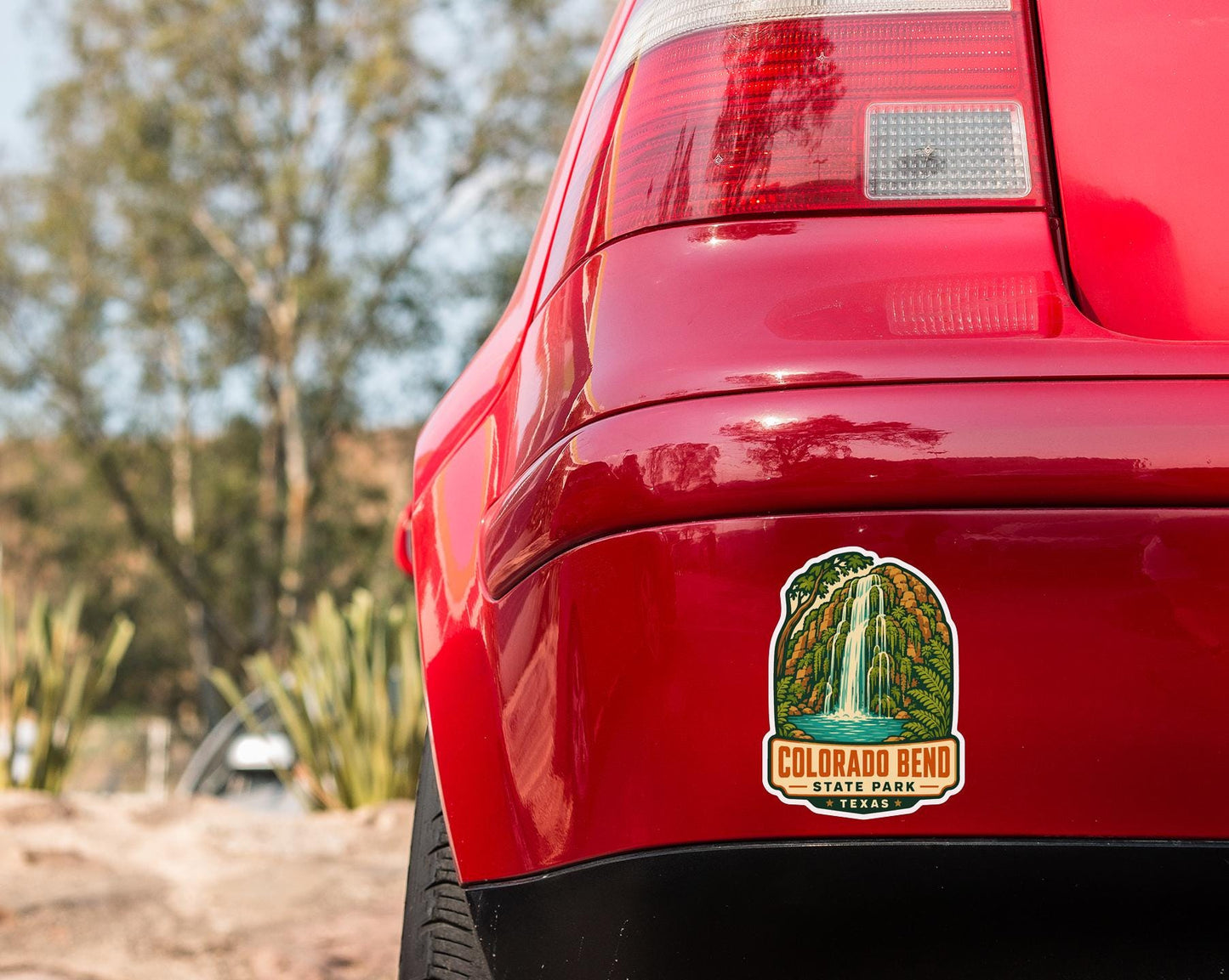 the rear end of a red car with a Colorado Bend State Park sticker on the trunk.