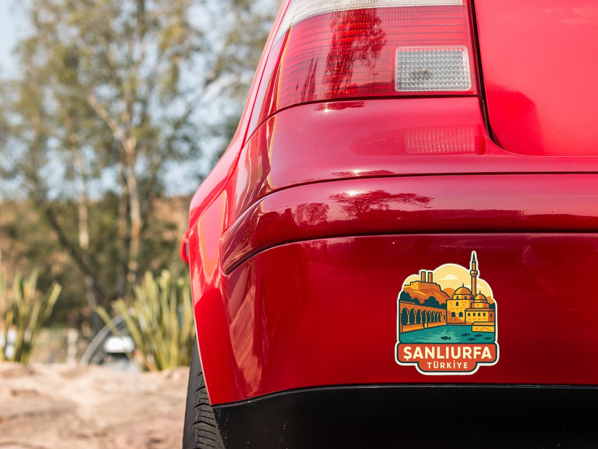 the rear end of a red car with a sticker on the trunk that features a scenic illustration of a city.