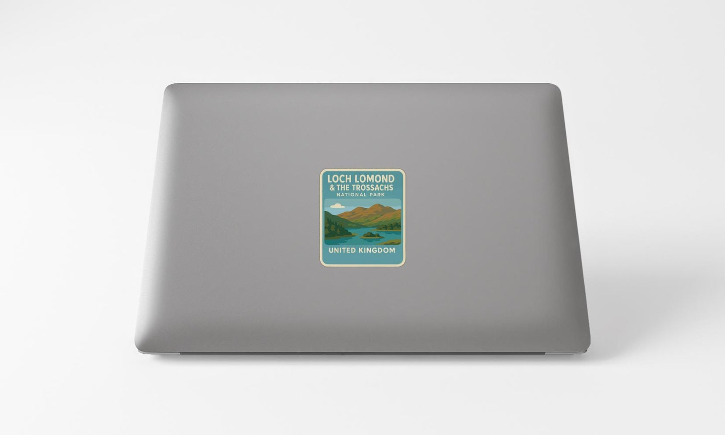 A sticker on the back of a laptop, depicting a scenic landscape with mountains, a lake, and a blue sky.