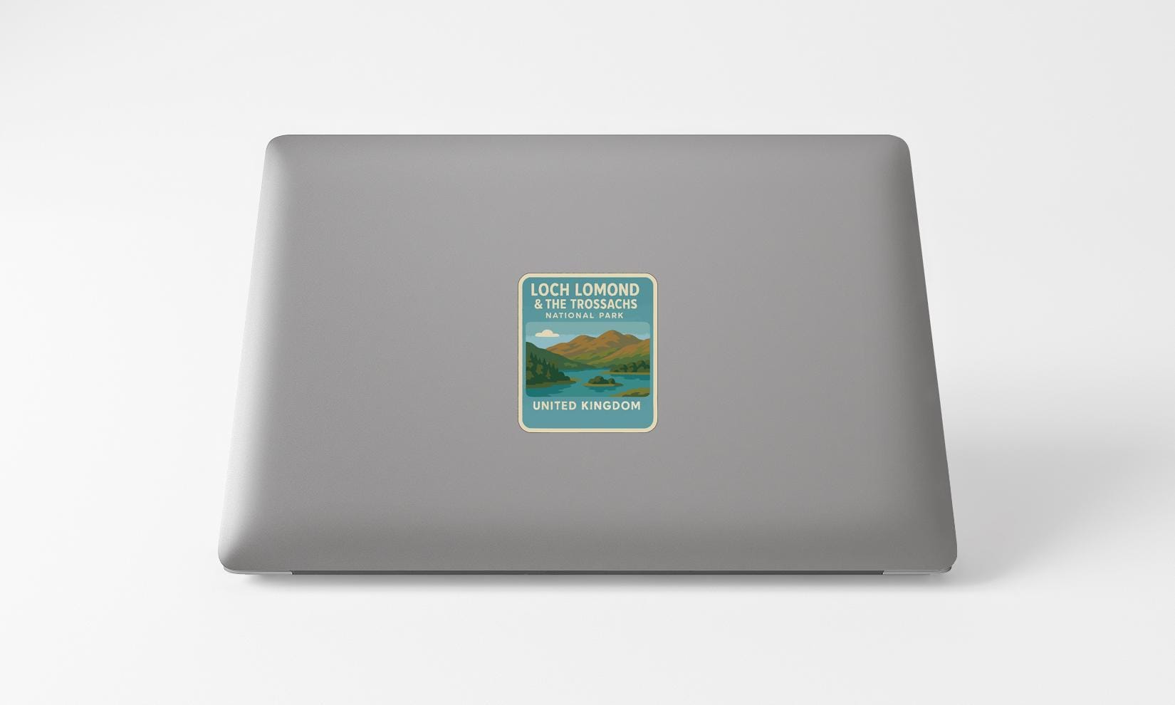 A sticker on the back of a laptop, depicting a scenic landscape with mountains, a lake, and a blue sky.