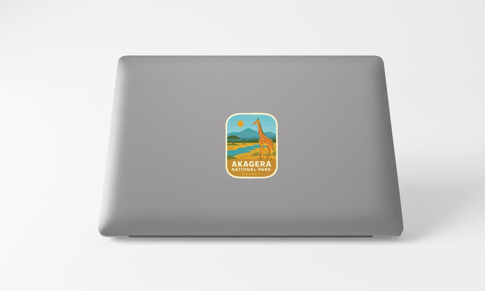 A sticker on the back of a laptop displaying a giraffe and a landscape with mountains.