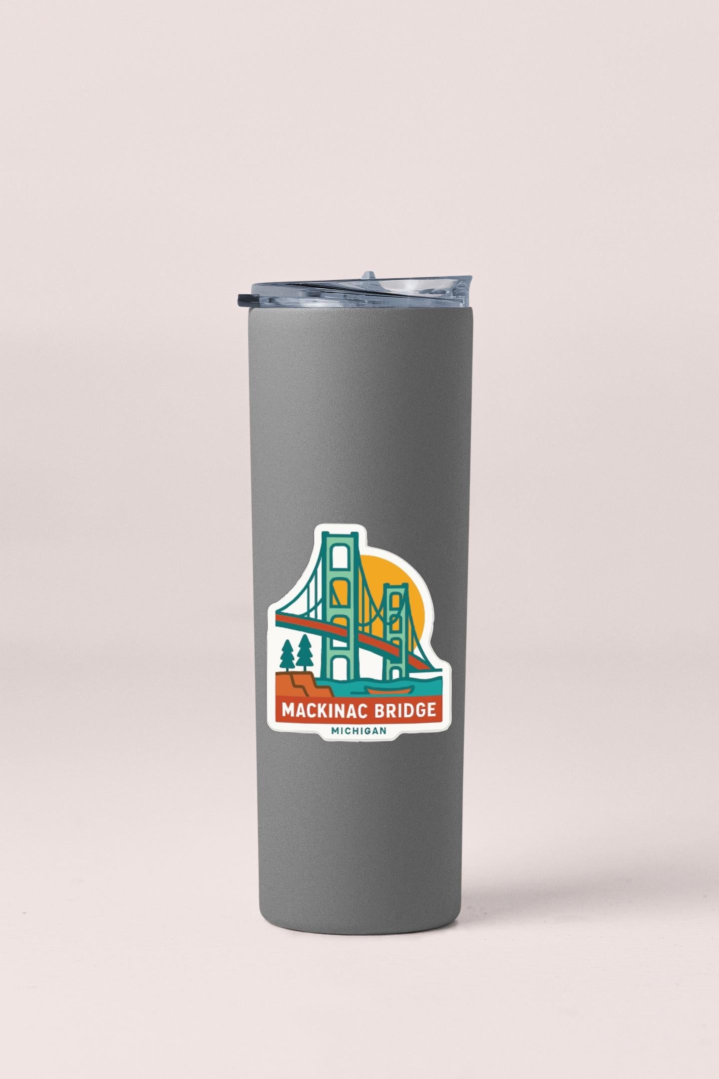 A gray insulated tumbler with a sticker depicting the Mackinac Bridge in Michigan.