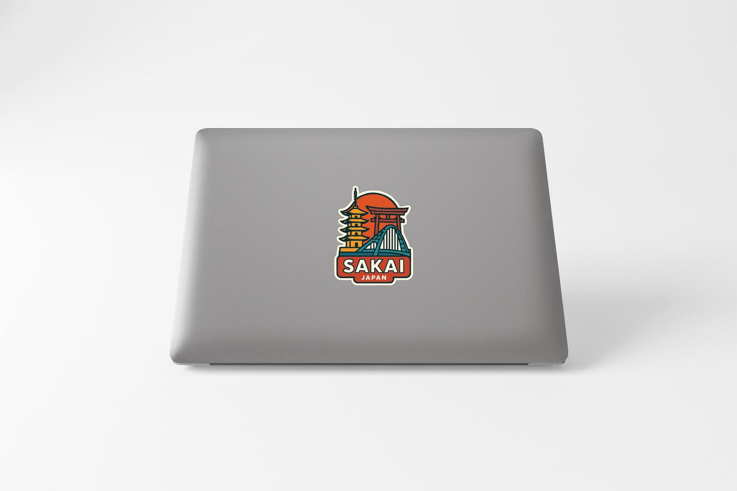 a sticker with a colorful illustration of a temple and the word "SAKAI" on the back of a laptop.
