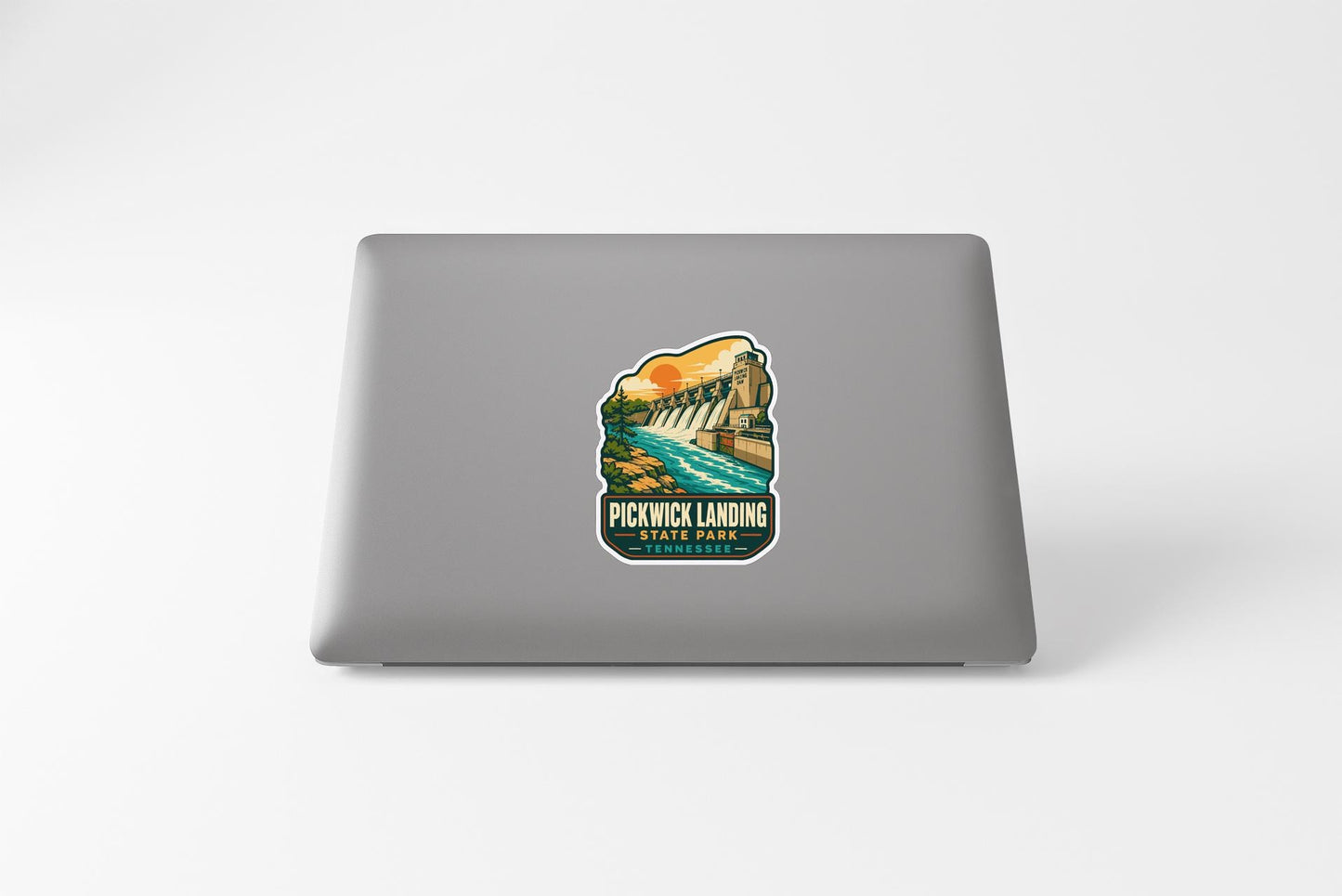 A sticker on the back of a laptop, depicting a scenic landscape with a waterfall and a bridge.
