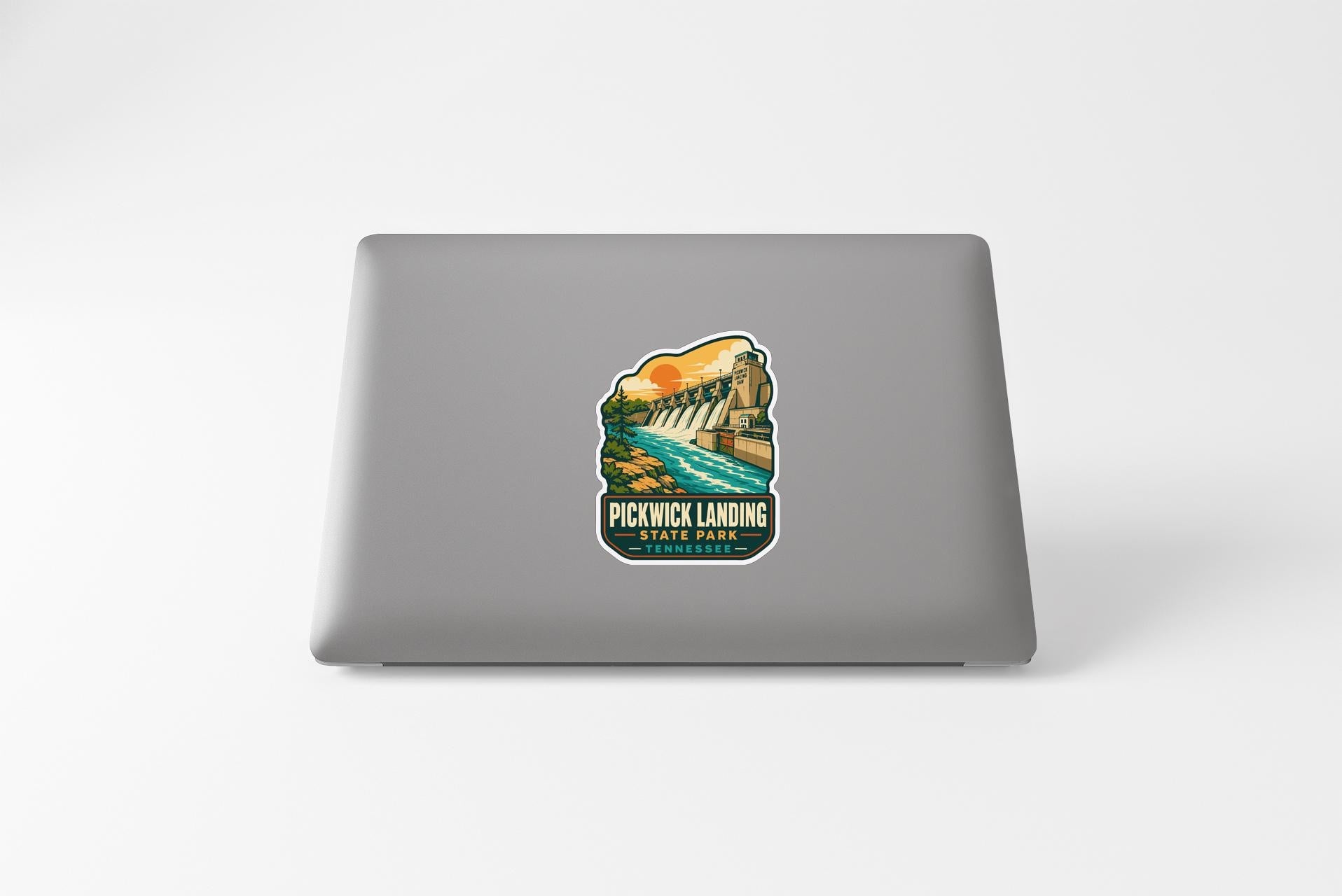 A sticker on the back of a laptop, depicting a scenic landscape with a waterfall and a bridge.