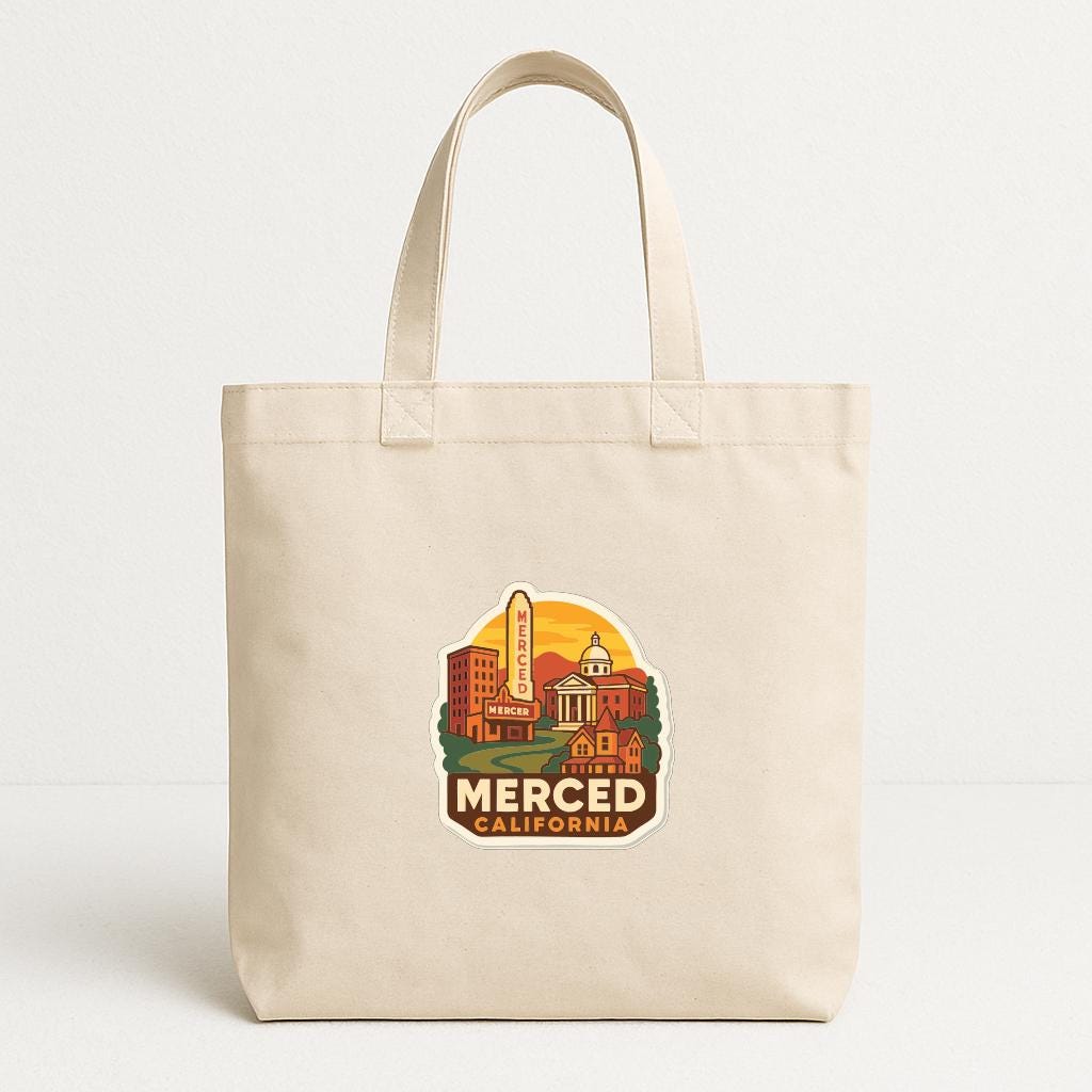 A beige tote bag with a printed design depicting a cityscape and the text "MERCED, CALIFORNIA" printed on it.